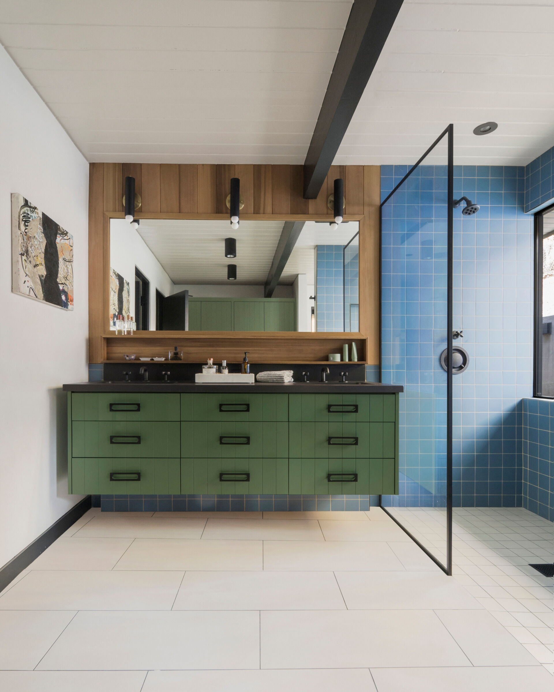 The primary bathroom uses ceramic tile for a clean, tactile floor surface. Custom cabinetry and a green vanity anchor the space, while blue wall tiles add a calming tone, extending the home's signature palette.