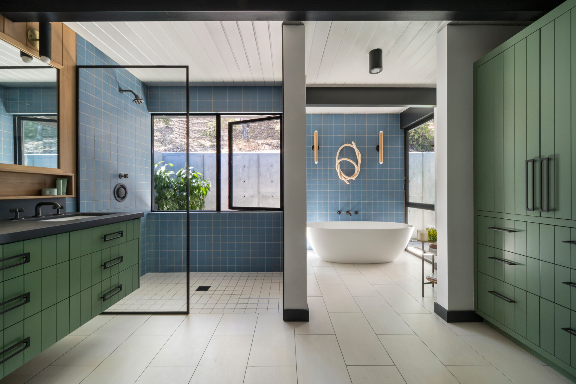 The primary bathroom uses ceramic tile for a clean, tactile floor surface. Custom cabinetry and a green vanity anchor the space, while blue wall tiles add a calming tone, extending the home's signature palette.