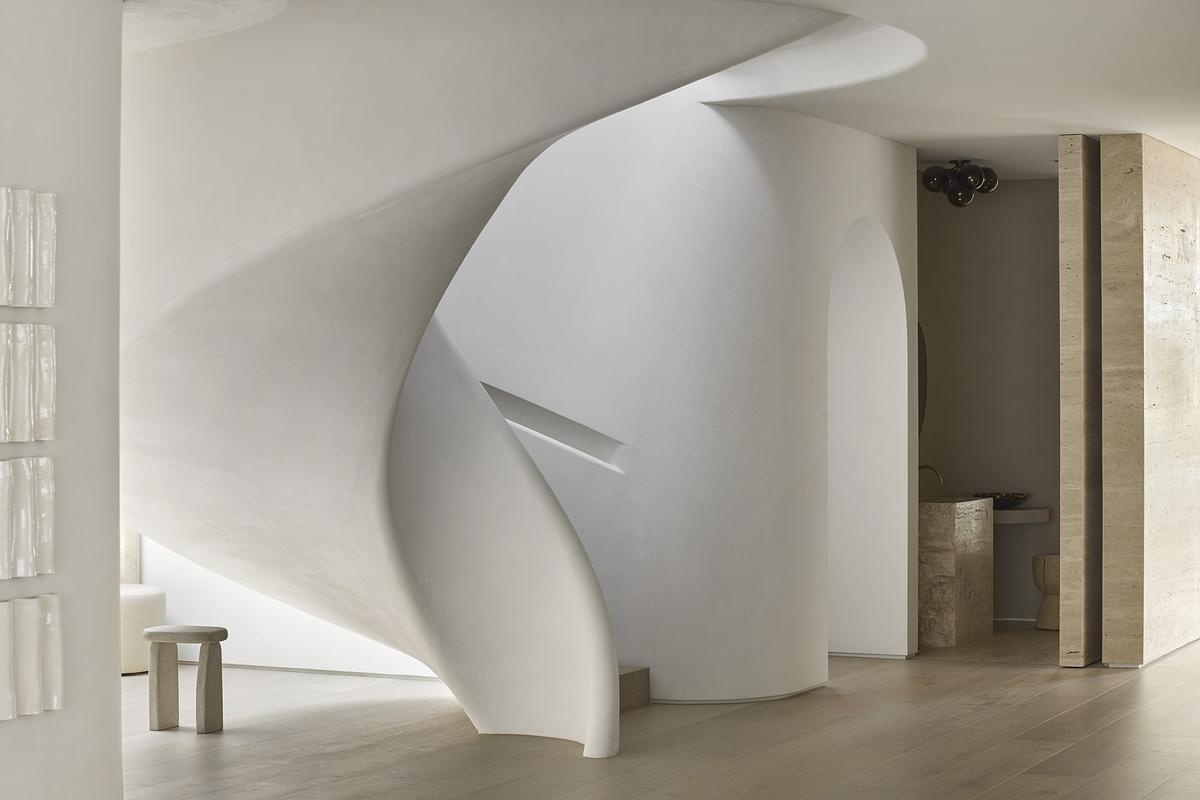 A sculptural spiral staircase in polished plaster anchors the home's interior, blending movement, form, and soft materiality.