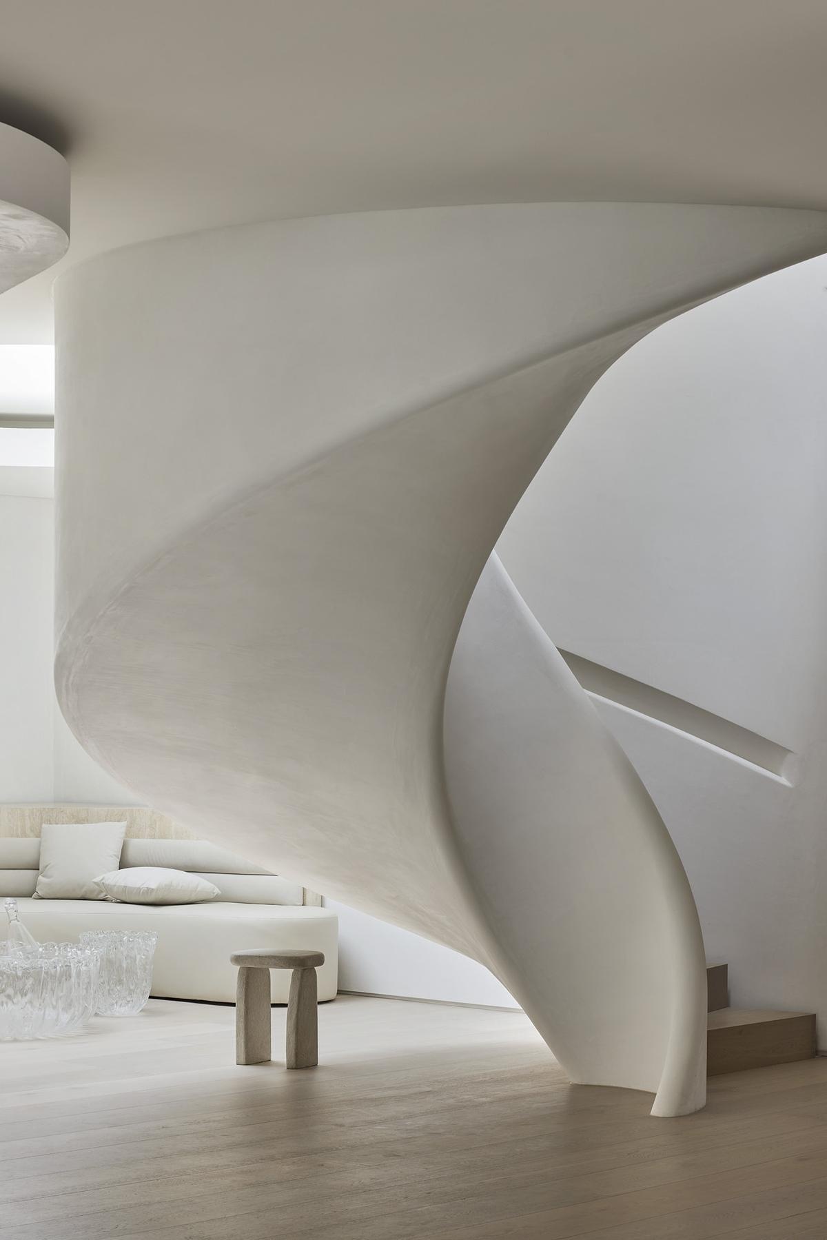 A sculptural spiral staircase in polished plaster anchors the home's interior, blending movement, form, and soft materiality.
