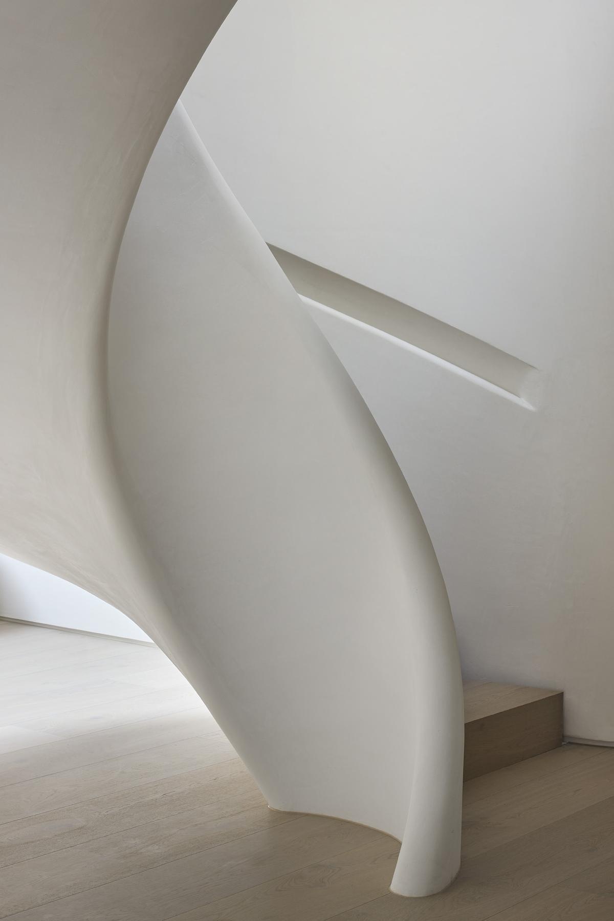 A sculptural spiral staircase in polished plaster anchors the home's interior, blending movement, form, and soft materiality.