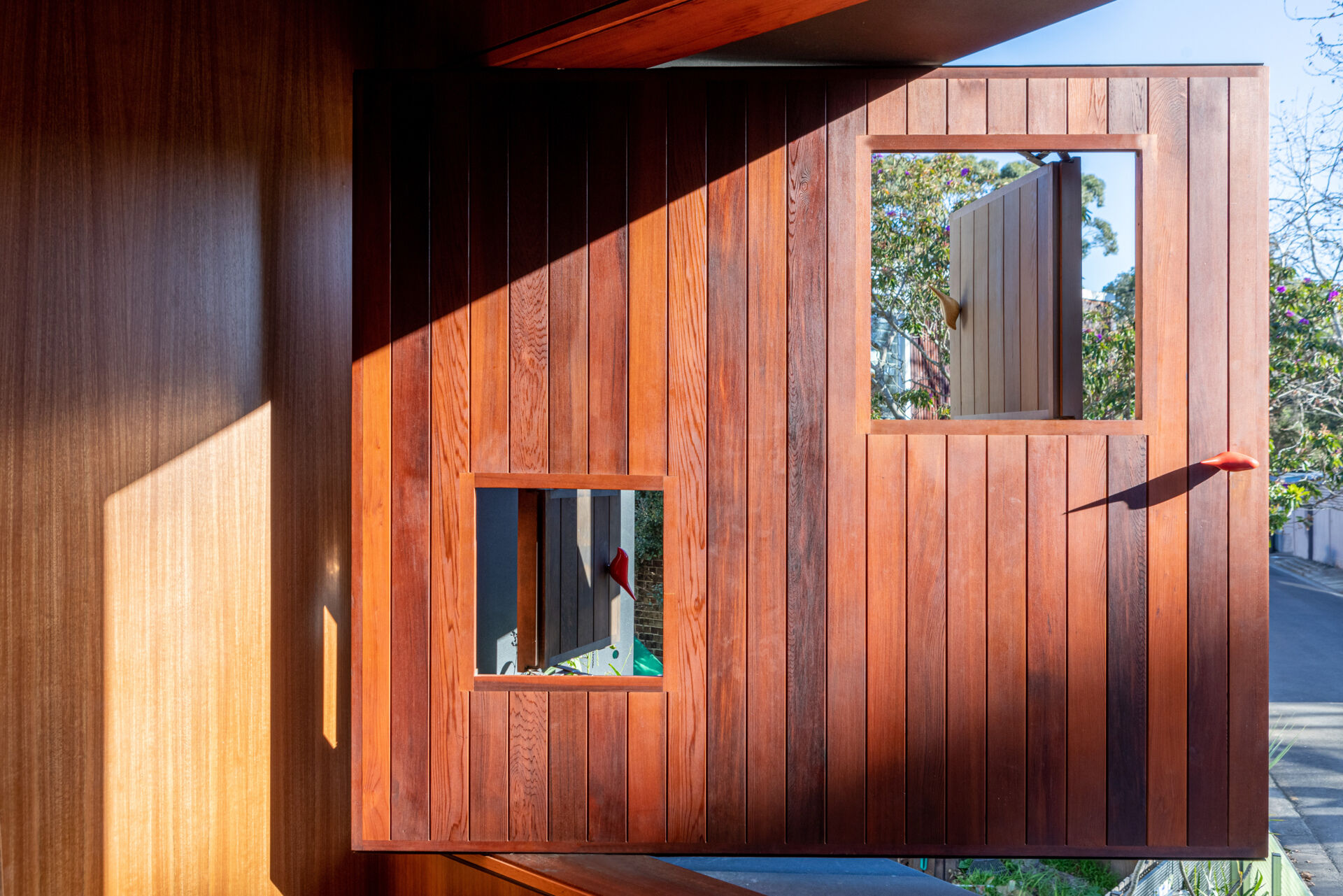 The private areas of the home, like this bedroom, feels warm and enveloping, with rich timber paneling covering every surface. Soft morning light filters through a pivoting window, offering views outside while preserving privacy.