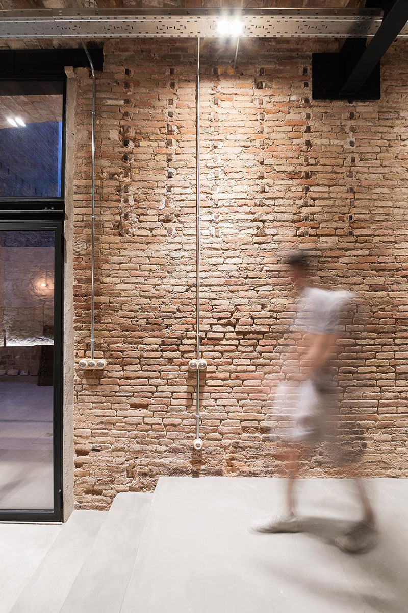 Original brick walls and a built-in sofa with colorful cushions leads to folding glass doors that open to a private courtyard, framed by decorative steel screens.
