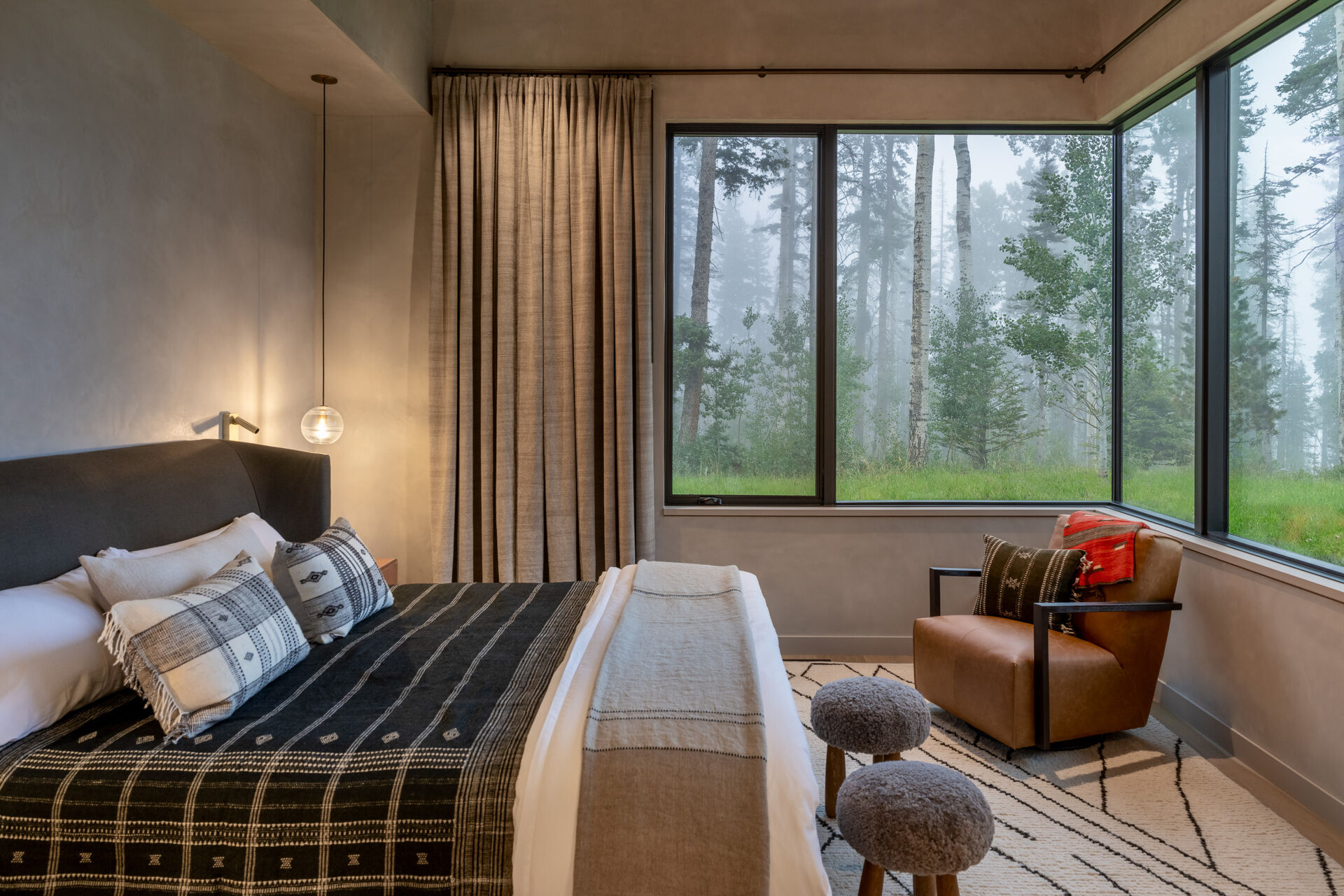 This bedroom frames the forest like living artwork, with large corner windows that open the space to misty mountain views. A soft palette of earthy tones keeps the atmosphere calm and grounding, while textured layers in the bedding add warmth and depth.