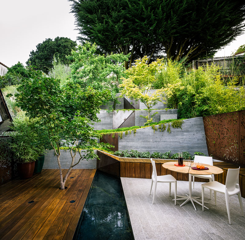 A narrow, sloped backyard is transformed into a Zen-like garden retreat with a winding ramp, concrete terraces, and layered plantings. It also features a reflecting pool, Japanese maples, and panoramic views.