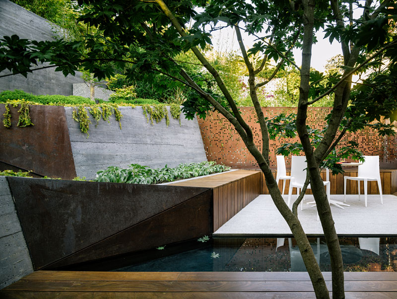 A narrow, sloped backyard is transformed into a Zen-like garden retreat with a winding ramp, concrete terraces, and layered plantings. It also features a reflecting pool, Japanese maples, and panoramic views.