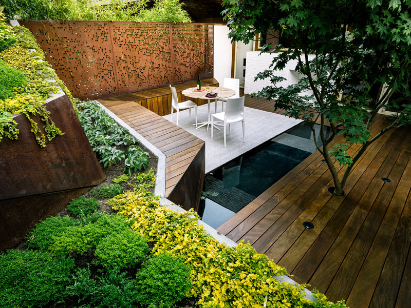 A narrow, sloped backyard is transformed into a Zen-like garden retreat with a winding ramp, concrete terraces, and layered plantings. It also features a reflecting pool, Japanese maples, and panoramic views.