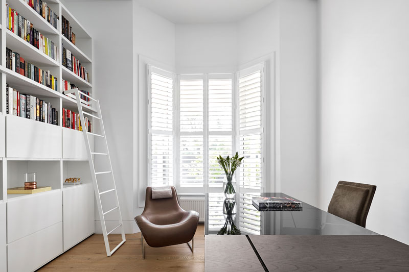 At the front of the home, a bright white office with wall-to-wall shelving provides a crisp and functional workspace.