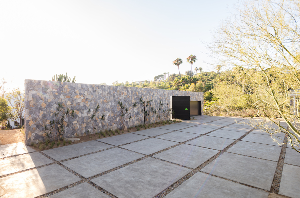 Approaching the house, old-world–inspired courtyards and custom stone walls create a sense of permanence. The driveway and surrounding hardscape lead visitors into a property that's revealed through a pivoting black door.