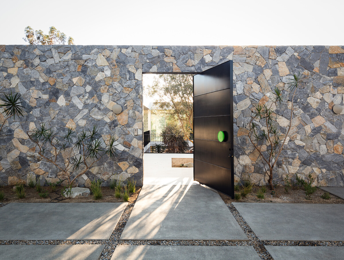 Approaching the house, old-world–inspired courtyards and custom stone walls create a sense of permanence. The driveway and surrounding hardscape lead visitors into a property that's revealed through a pivoting black door.