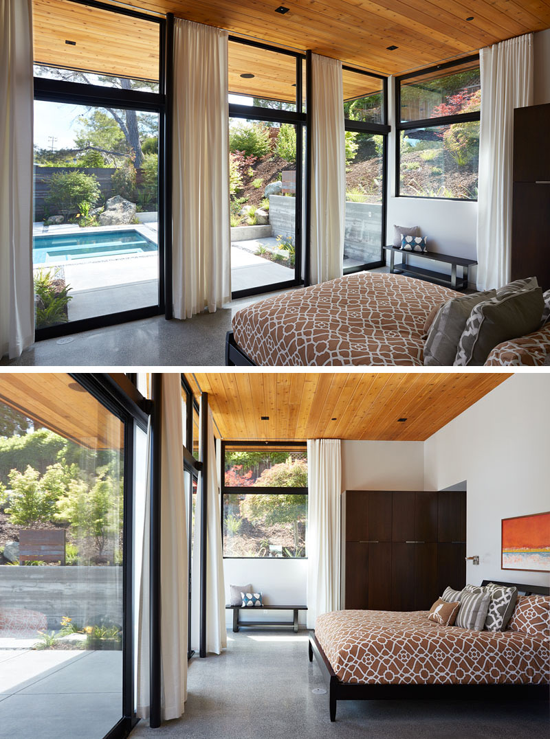 In this bedroom, floor-to-ceiling windows frame backyard views and a warm wood ceiling extends seamlessly outdoors.