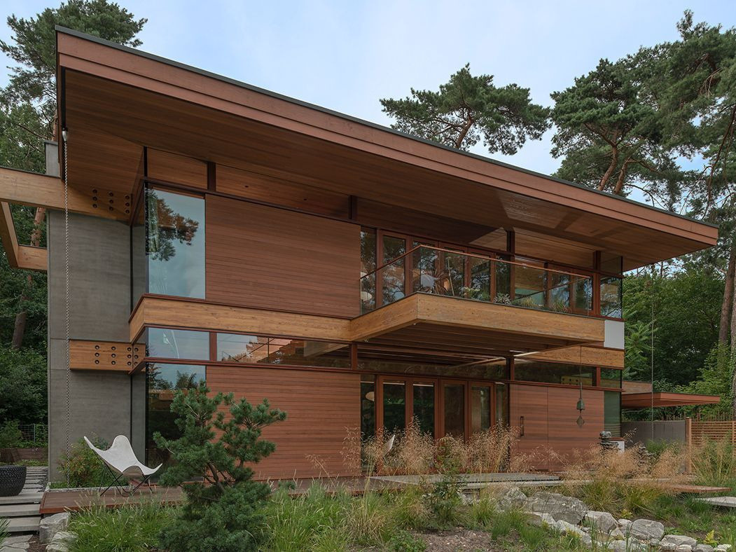 The design of this home includes expansive glass walls that invite the outdoors in, while natural wood tones and warm materials soften the geometry, creating a sense of welcome from the very first glance.