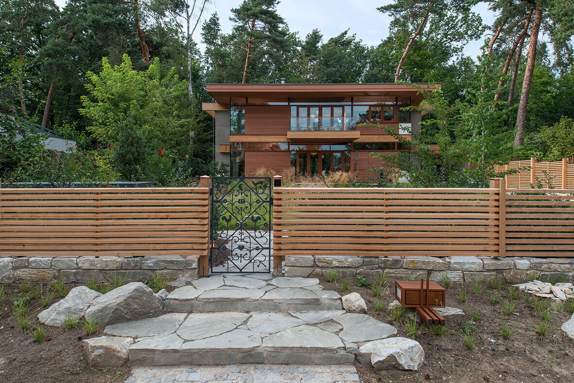 The design of this home includes expansive glass walls that invite the outdoors in, while natural wood tones and warm materials soften the geometry, creating a sense of welcome from the very first glance.