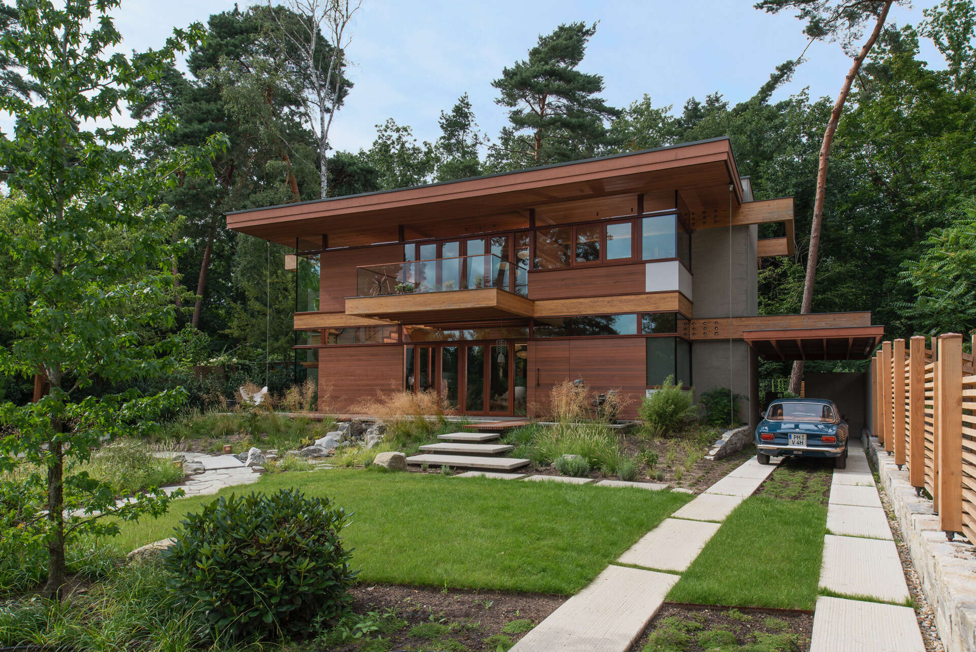 The design of this home includes expansive glass walls that invite the outdoors in, while natural wood tones and warm materials soften the geometry, creating a sense of welcome from the very first glance.