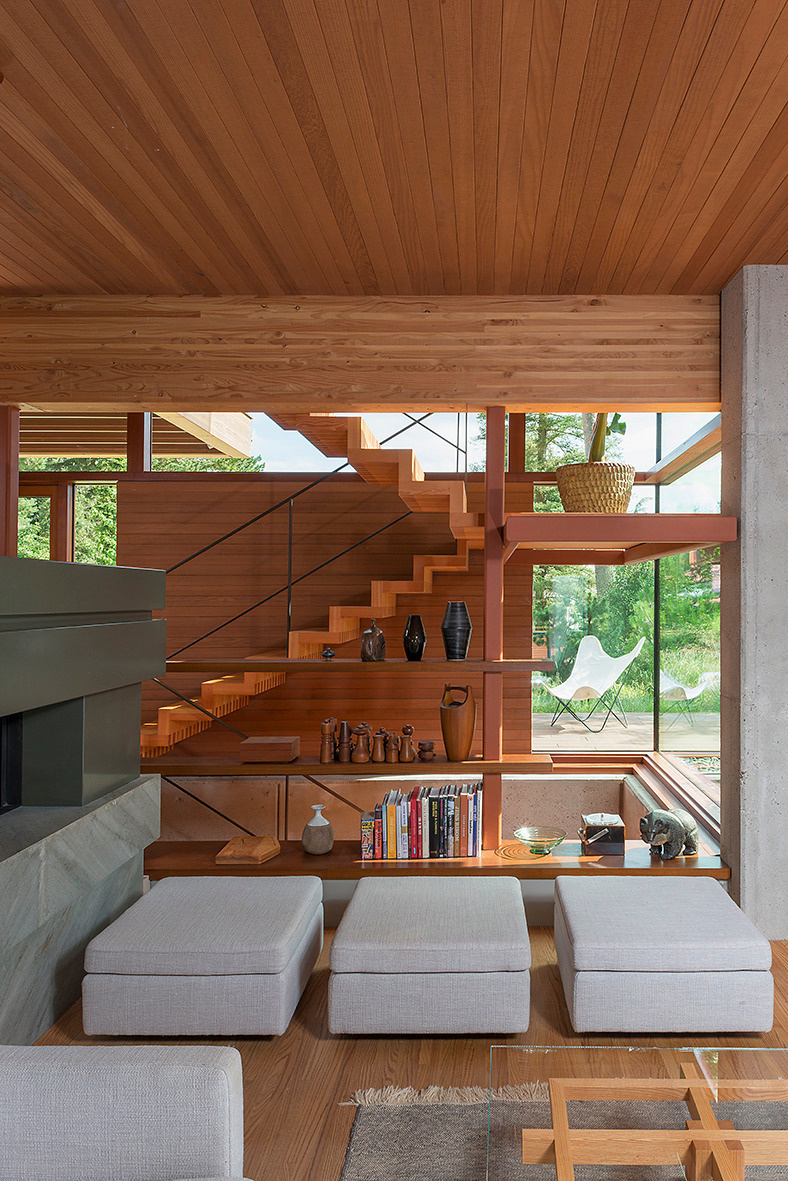 This living room revolves around a double-sided fireplace, providing both visual drama and cozy warmth. The space feels open yet intimate, thanks to the balance of large windows, exposed structural elements, and careful furniture placement.