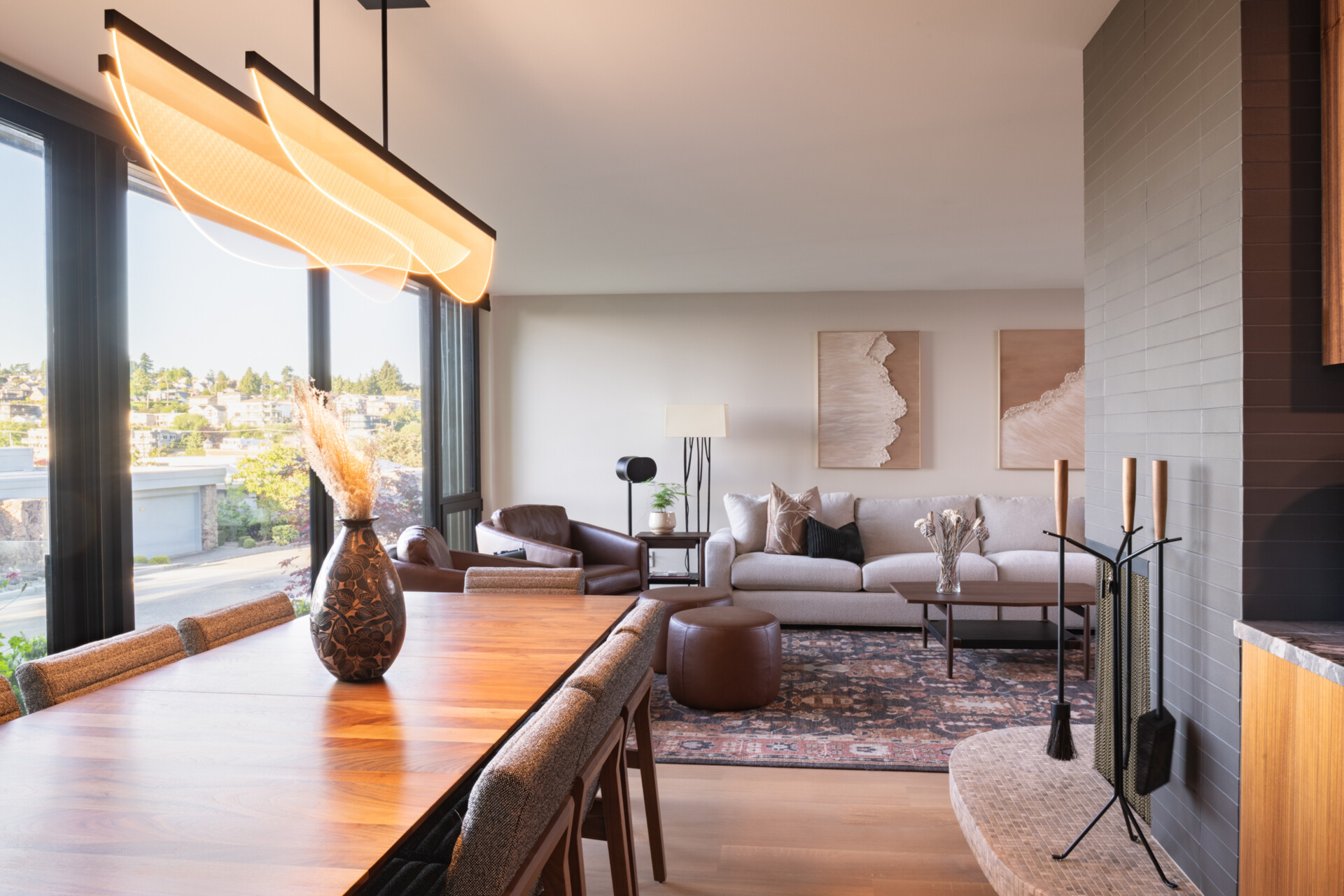 The open living and dining area flows directly from the kitchen, framed by glass walls that draw in the surrounding landscape. The original fireplace anchors the room, while the updated finishes provide a fresh backdrop for gatherings. The effect is seamless continuity between past and present.
