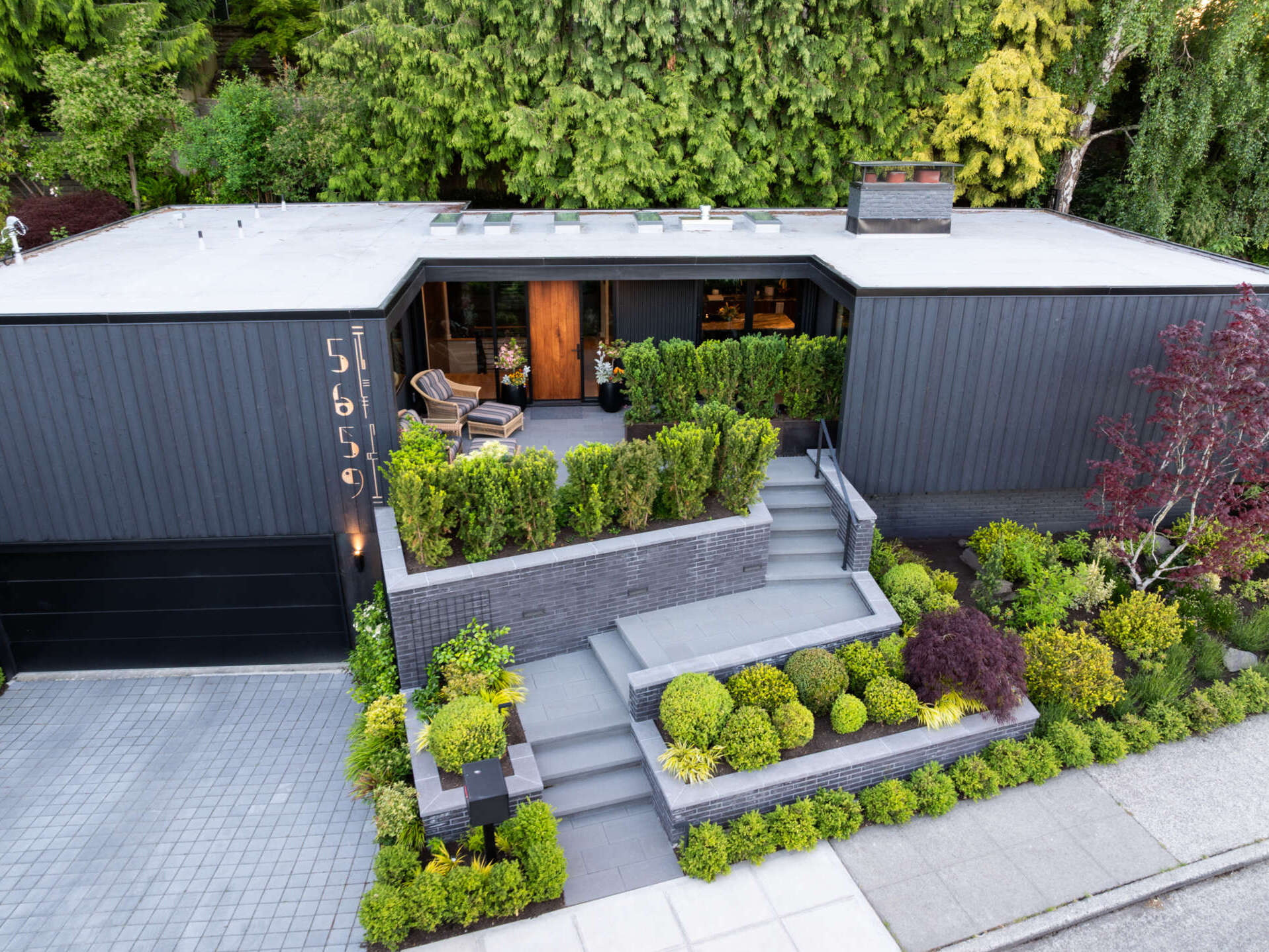 The bold shou sugi ban siding of this renovated mid-century modern home contrasts with the lush landscaping, while a pathway of stairs weaves through greenery to a welcoming patio.