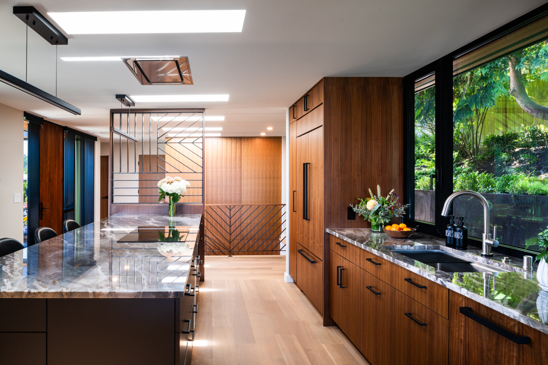 Warm walnut cabinetry, quartz countertops, and geometric metalwork add depth and character to this kitchen. Multiple skylights flood the space with natural light, making it both practical and inviting.