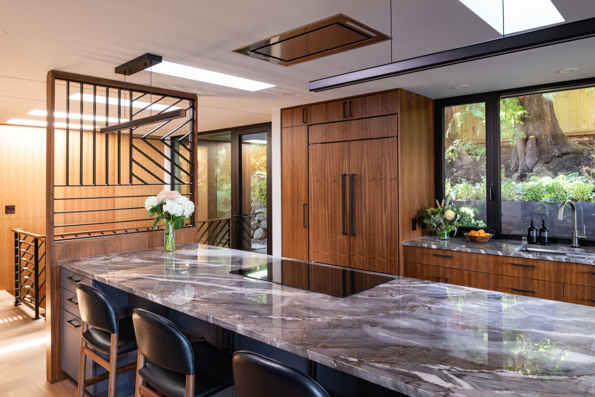Warm walnut cabinetry, quartz countertops, and geometric metalwork add depth and character to this kitchen. Multiple skylights flood the space with natural light, making it both practical and inviting.