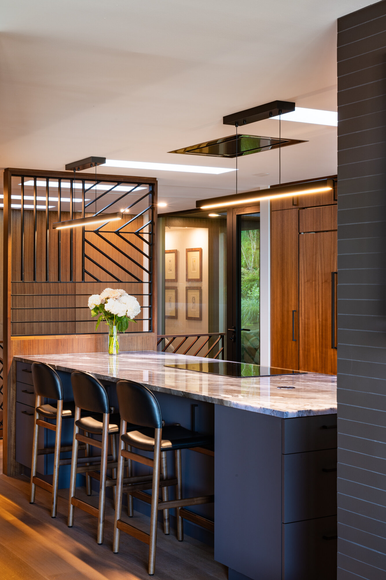 Warm walnut cabinetry, quartz countertops, and geometric metalwork add depth and character to this kitchen. Multiple skylights flood the space with natural light, making it both practical and inviting.