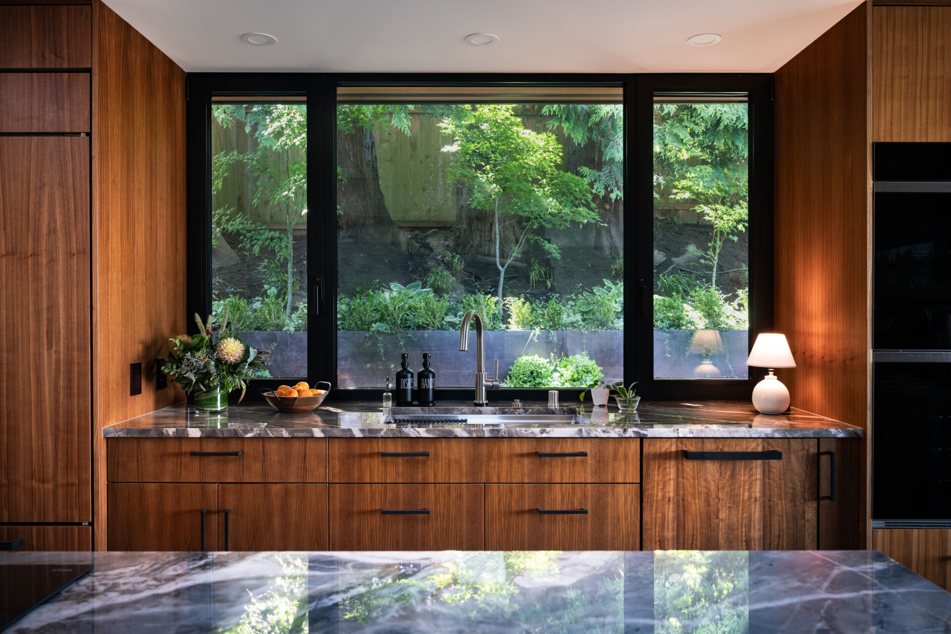 Warm walnut cabinetry, quartz countertops, and geometric metalwork add depth and character to this kitchen. Multiple skylights flood the space with natural light, making it both practical and inviting.