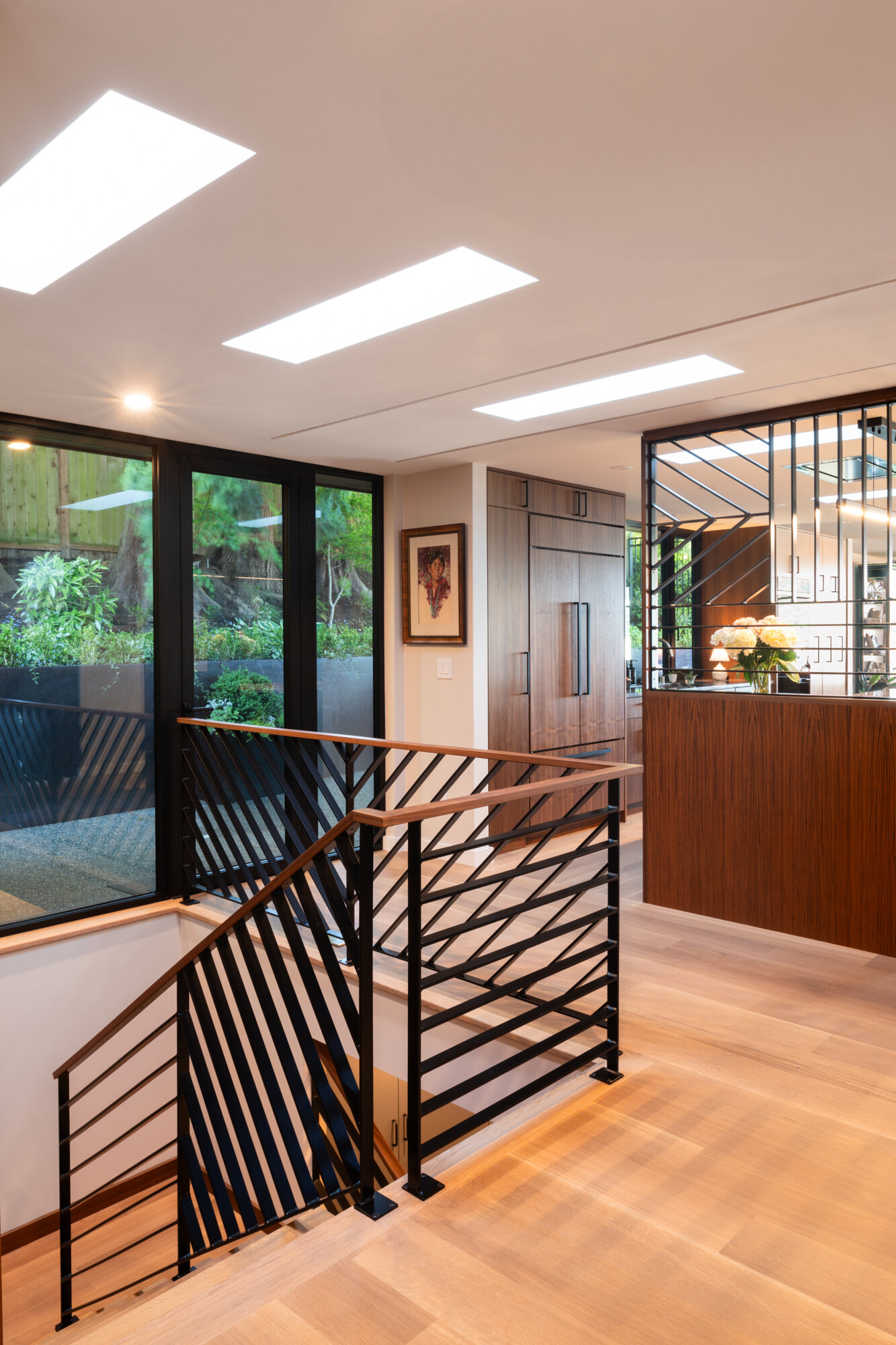 Stairs connects the main level to the lower floor of this renovated mid-century modern home, and introduce new touches, like the black metal railings with a geometric diagonal pattern, topped with warm wood handrails.