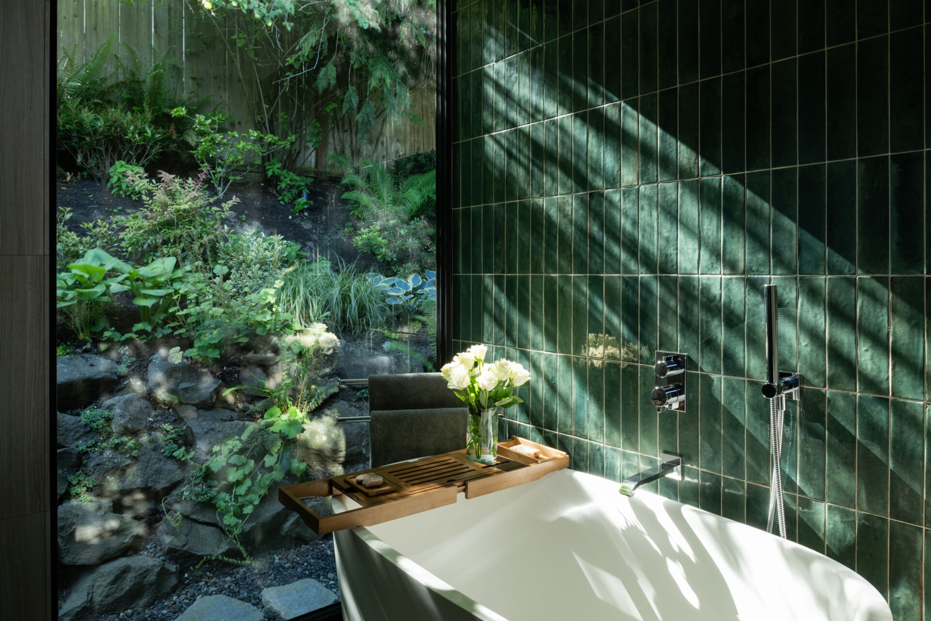 A spa-like bathroom in the primary suite completes the renovation’s story. Clean lines, vertical green tiles, and a view of nature create a calming atmosphere that feels indulgent without being overpowering.