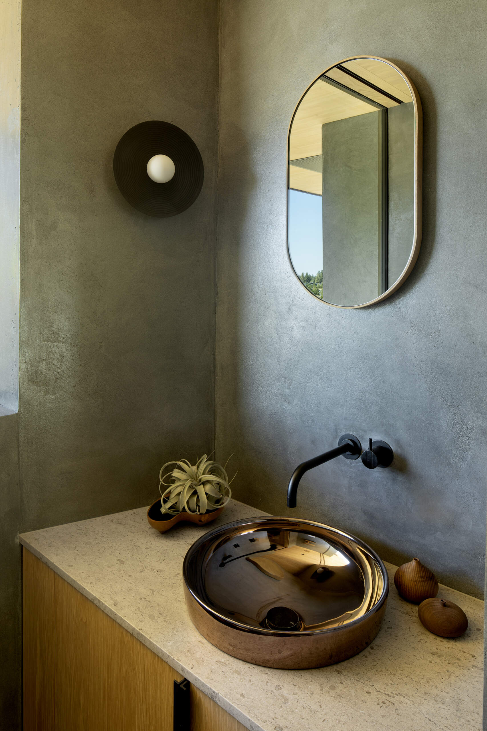 A powder room with a wood vanity, stone countertop, and metallic basin.