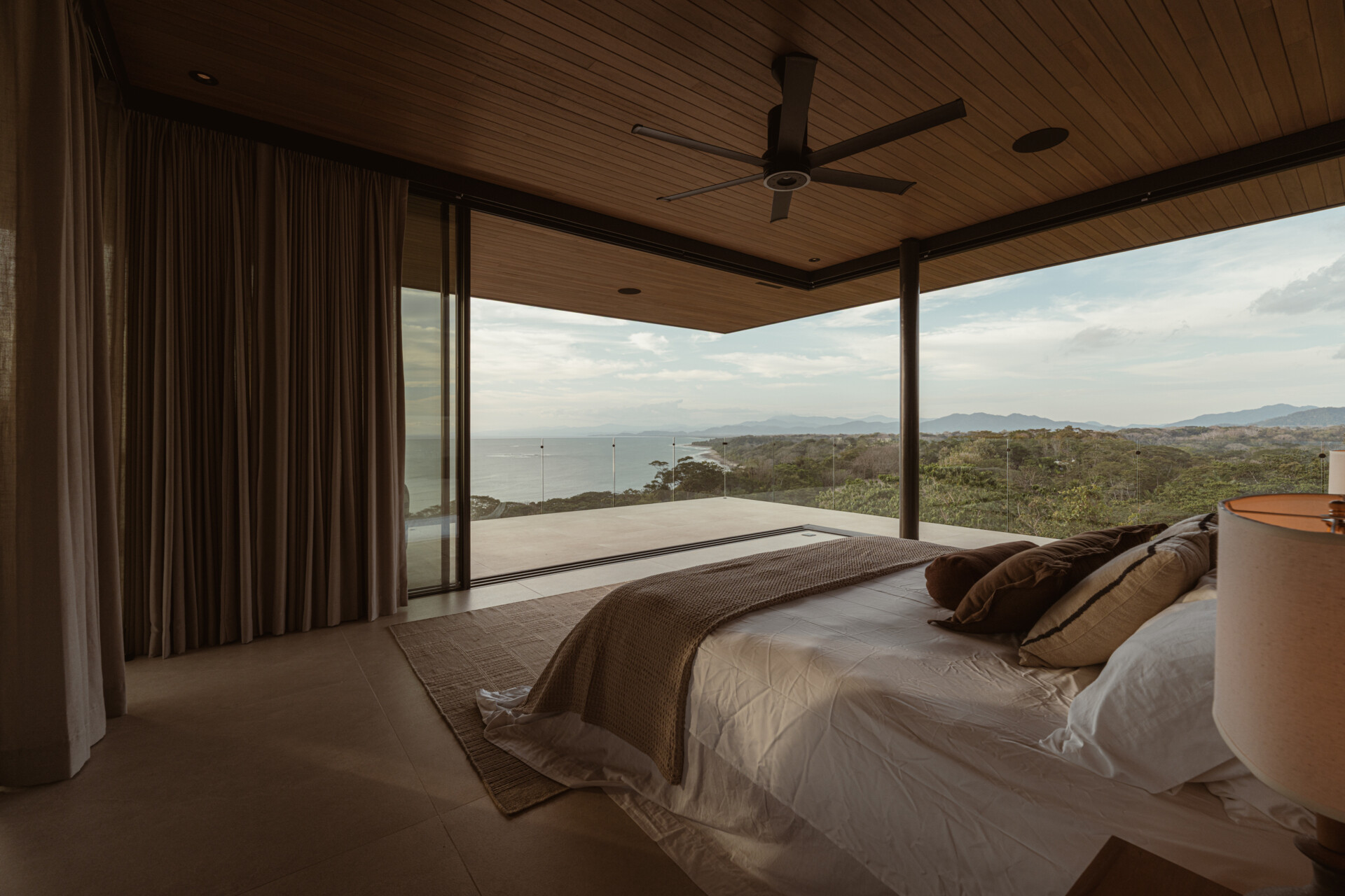 Warm earth tones and layered textures give this bedroom and its ensuite a peaceful quality. The bedroom features a soft beige headboard with subtle geometric stitching, paired with woven wood panels and detailed nightstands that add a handcrafted touch. 