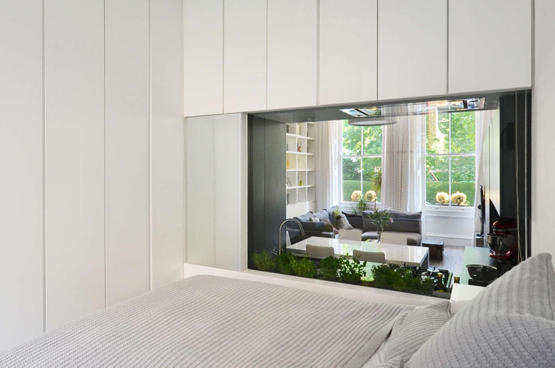 A glass backsplash in the kitchen offers a surprising view into the bedroom while filling the home with natural light. Privacy is just a screen away in this unique bedroom-to-kitchen window design.