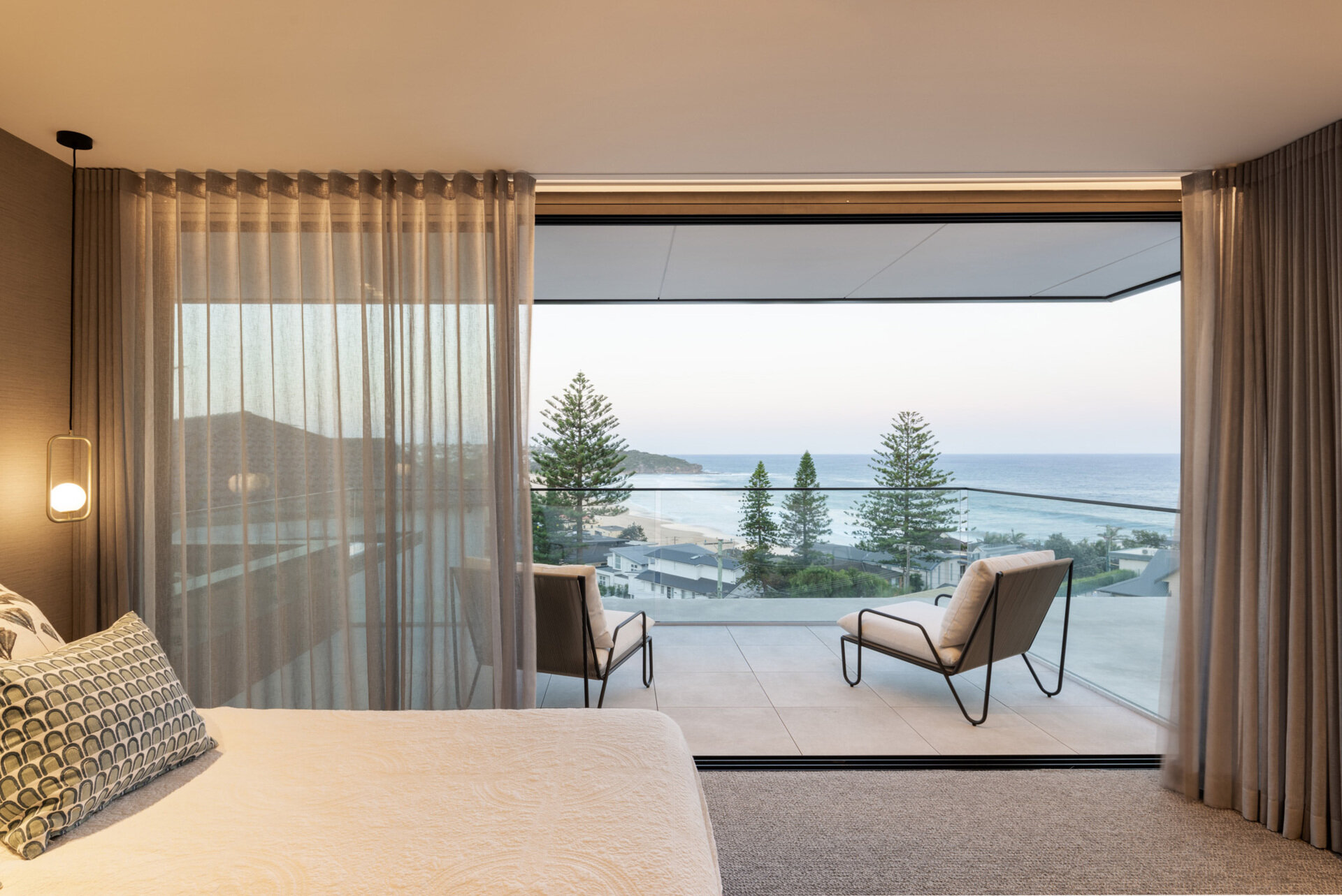 This primary bedroom enjoys a private balcony that captures an elevated view over Curl Curl beach, secluded yet still connected to the ever-present beachscape.