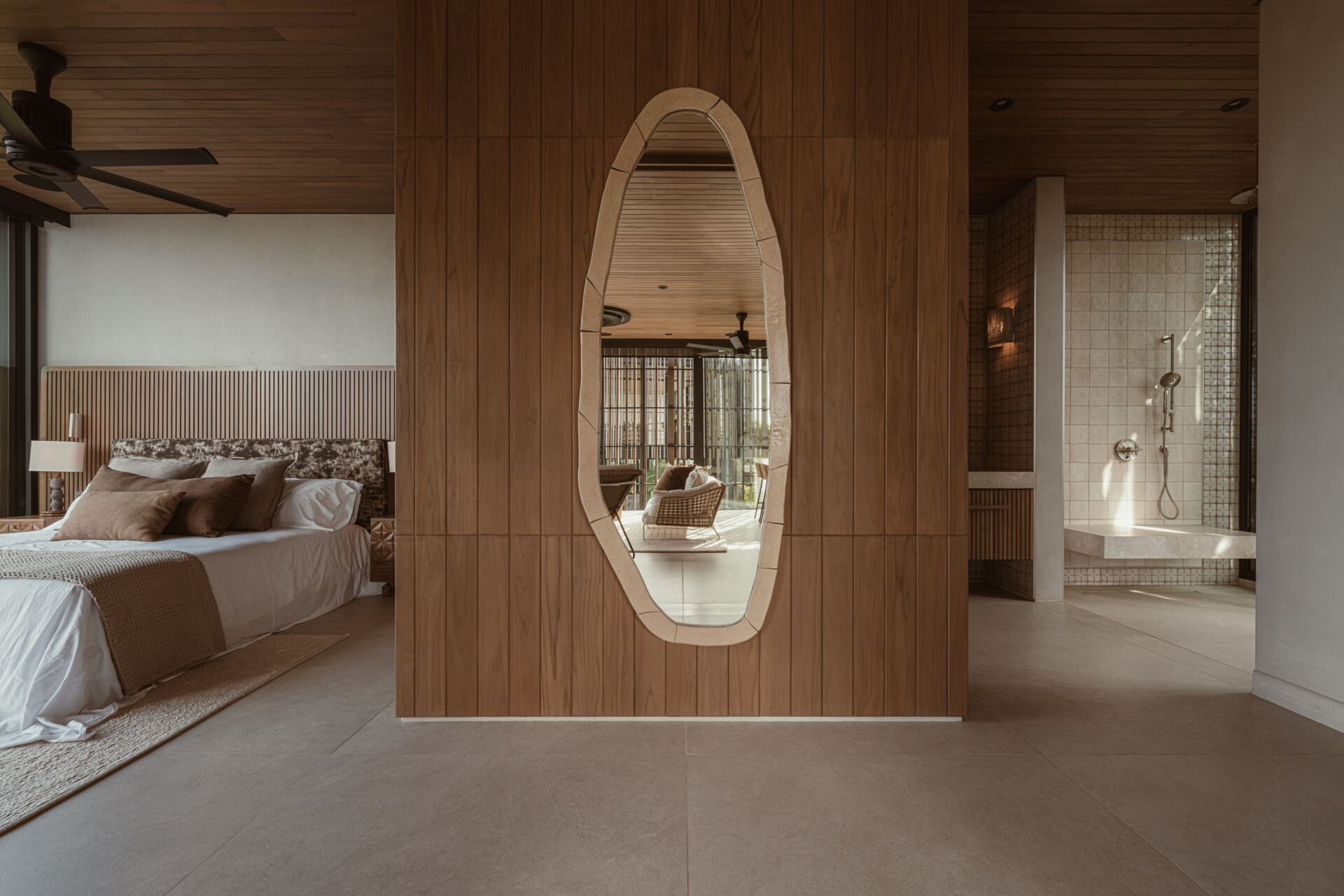 Natural materials lead the experience in this bedroom: reforested teak clads the ceiling and feature wall, while earthy stone flooring and soft woven textures ground the space. 