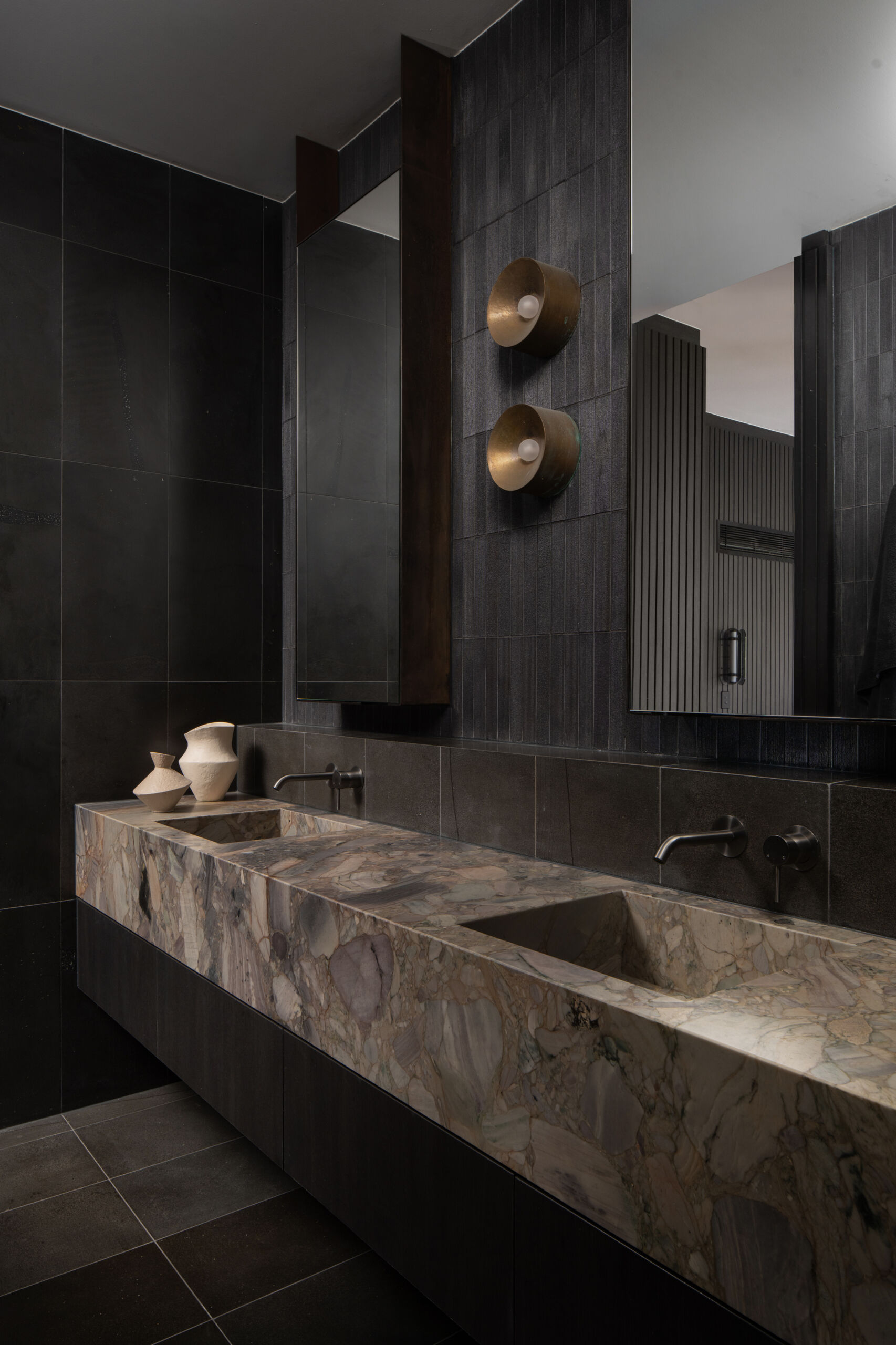 This bathroom pairs natural textures with clean, modern lines to create a serene retreat. Deep charcoal tiles wrap the walls and floor, their muted sheen reflecting daylight from a wide window that frames the surrounding greenery. 