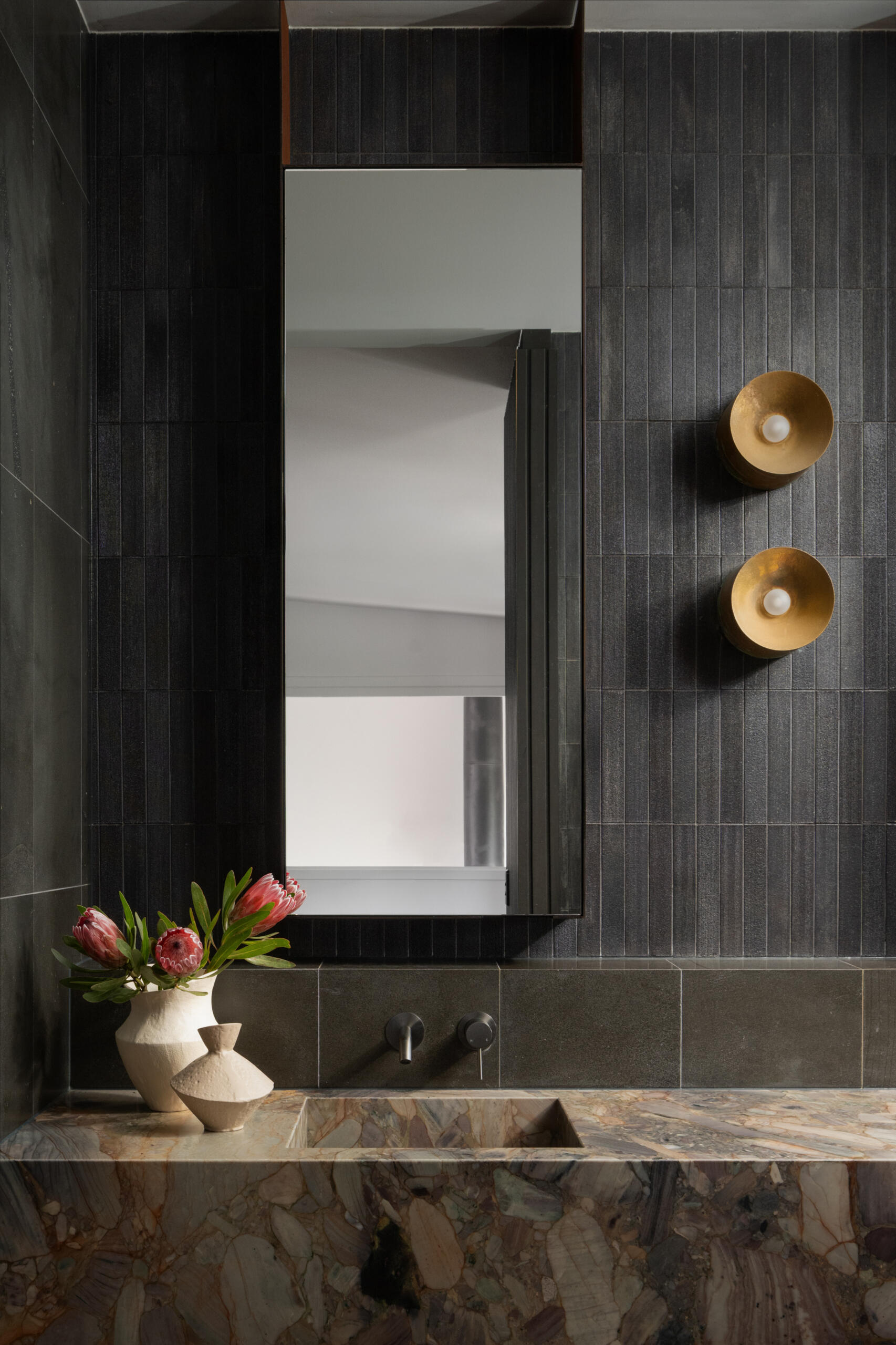 This bathroom pairs natural textures with clean, modern lines to create a serene retreat. Deep charcoal tiles wrap the walls and floor, their muted sheen reflecting daylight from a wide window that frames the surrounding greenery. 