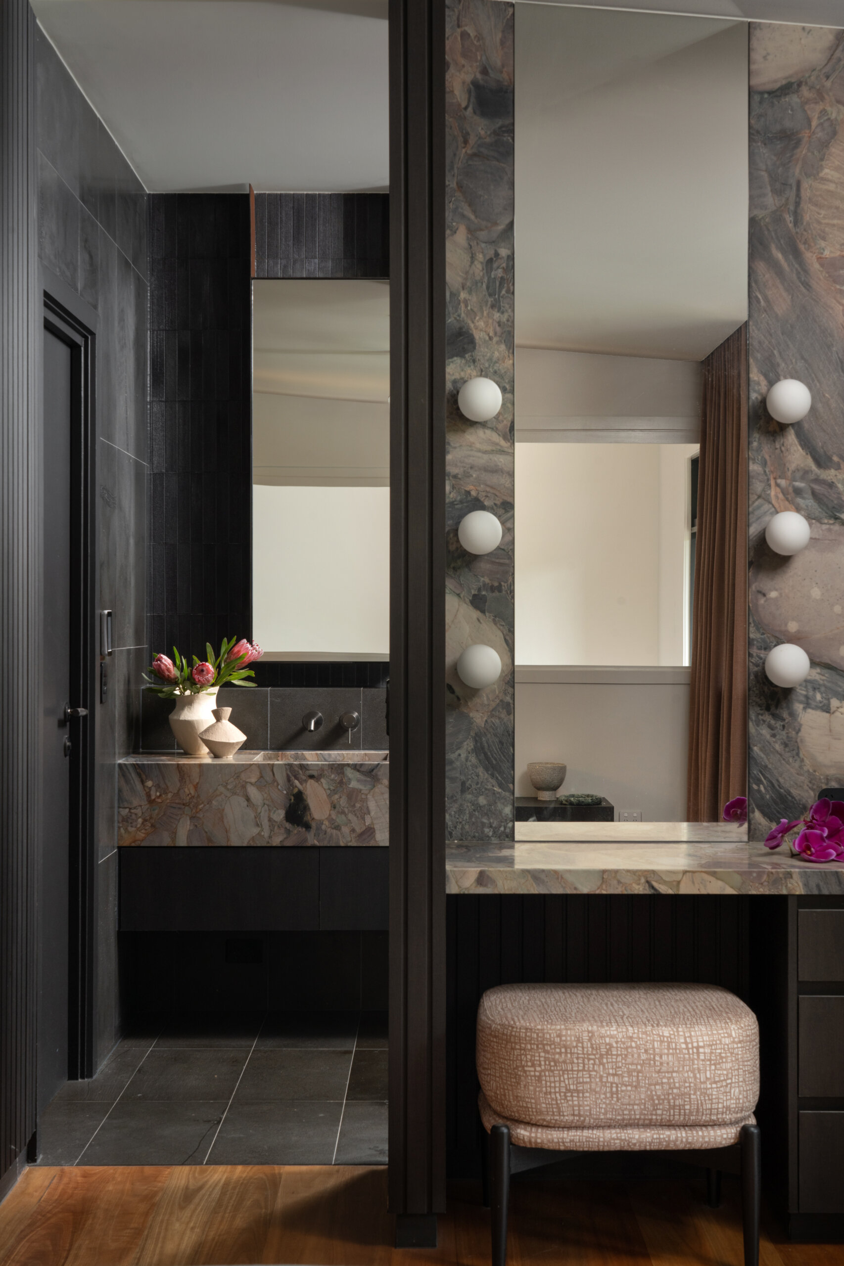 This bathroom pairs natural textures with clean, modern lines to create a serene retreat. Deep charcoal tiles wrap the walls and floor, their muted sheen reflecting daylight from a wide window that frames the surrounding greenery. 