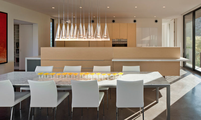 Pendant lights float above the dining table, anchoring the room with soft elegance. The adjacent kitchen is finished in light wood cabinetry and white countertops, striking a balance between modern simplicity and natural warmth.