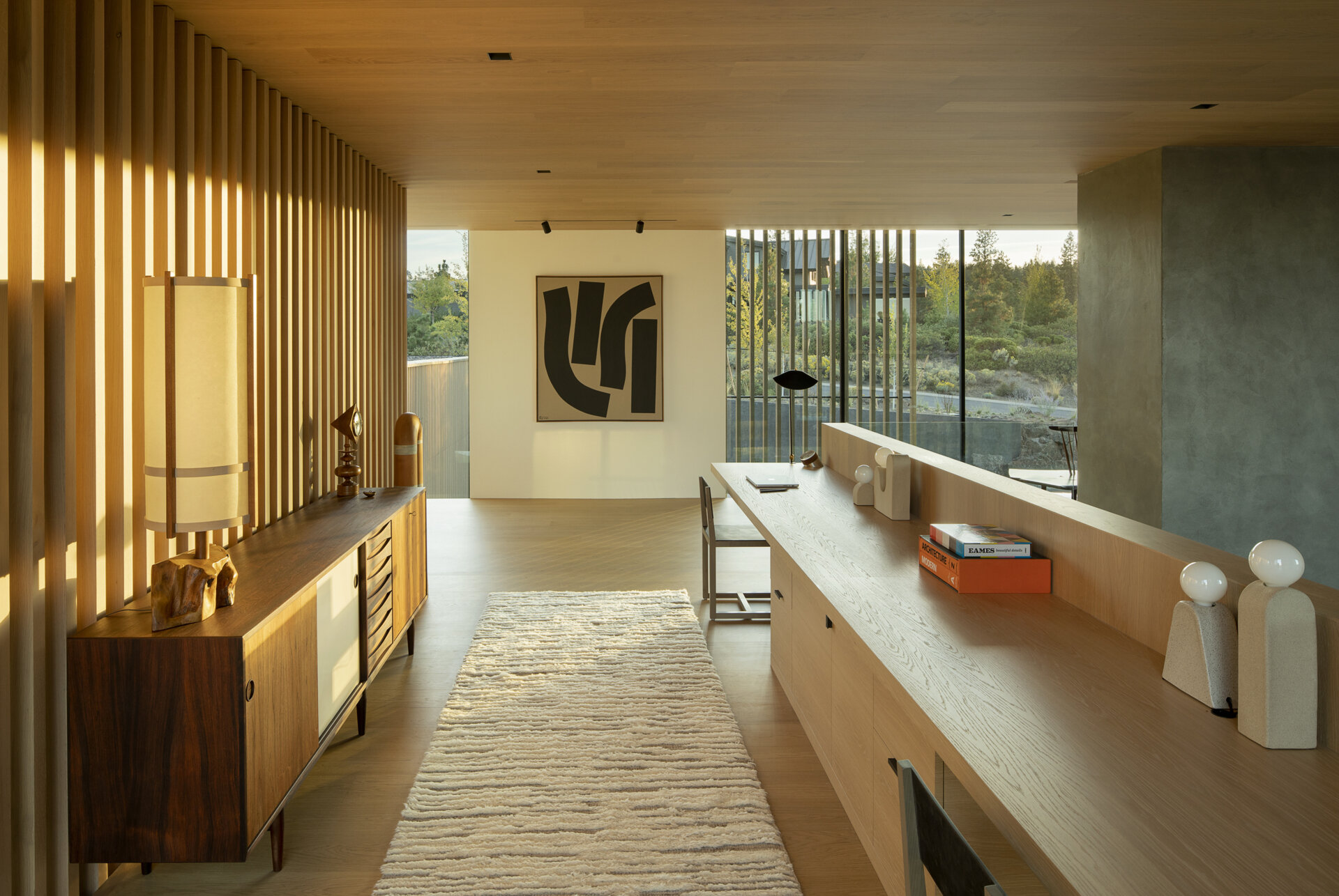 On the upper level of this modern home, an open workspace with built-in desk overlooks the living room, doubling as a quiet sitting area. It offers a serene spot for creativity, framed by the home’s gallery-like interiors.