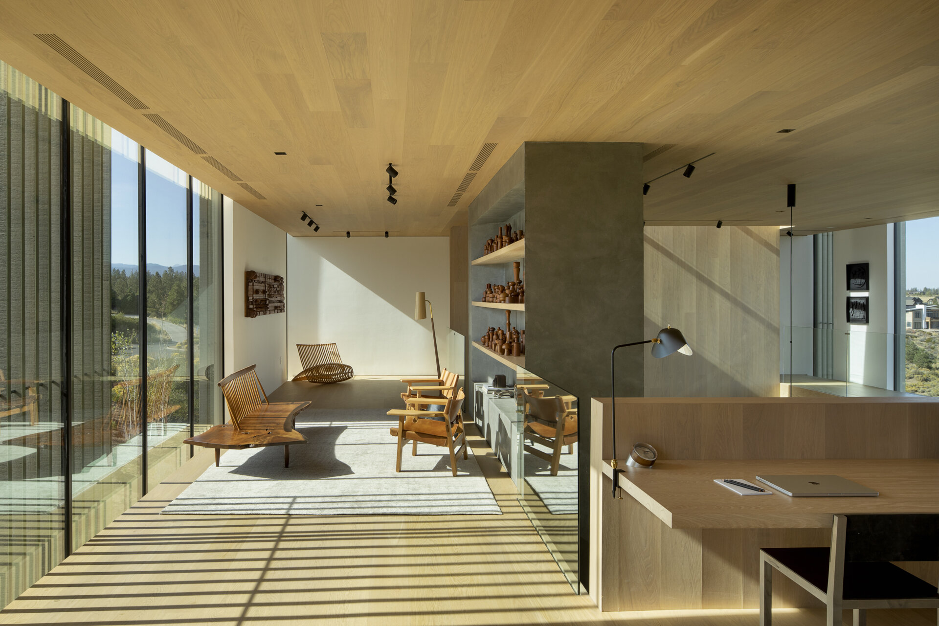 On the upper level of this modern home, an open workspace with built-in desk overlooks the living room, doubling as a quiet sitting area. It offers a serene spot for creativity, framed by the home’s gallery-like interiors.