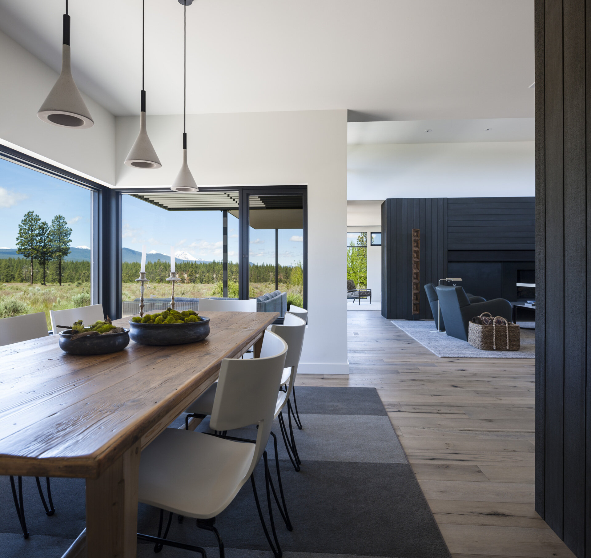 This dining area features a picture window that frames the tree views, while a solid wood table and chairs are anchored by a grey rug. Overhead, a trio pendant lights add a modern touch.