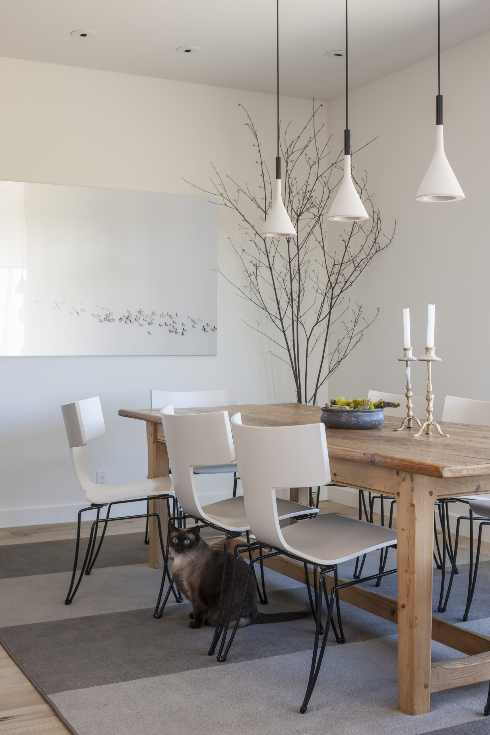 This dining area features a picture window that frames the tree views, while a solid wood table and chairs are anchored by a grey rug. Overhead, a trio pendant lights add a modern touch.