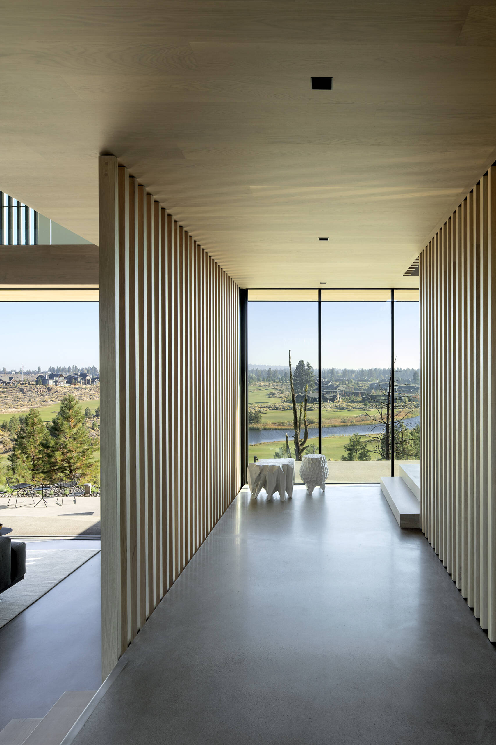 A large patinated steel pivot door welcomes visitors beneath the overhang, opening into an intermediate level with framed eastern views and a tactile connection to the outdoors.