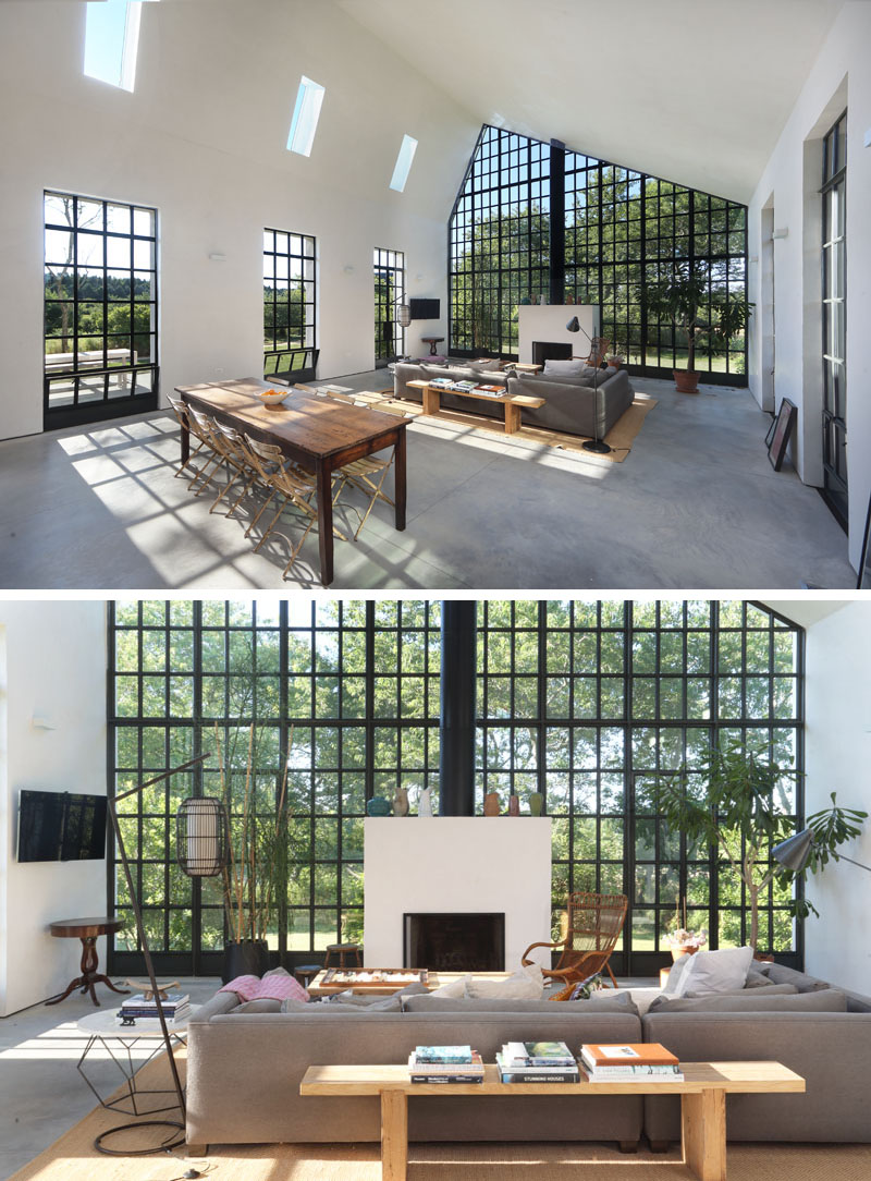 This open plan interior, with black framed windows, is arranged around a fireplace. The dining space extends from this area, placed directly in line with a side window for natural light and views. A white partition wall neatly separates this zone from the kitchen and a bathroom tucked behind it.