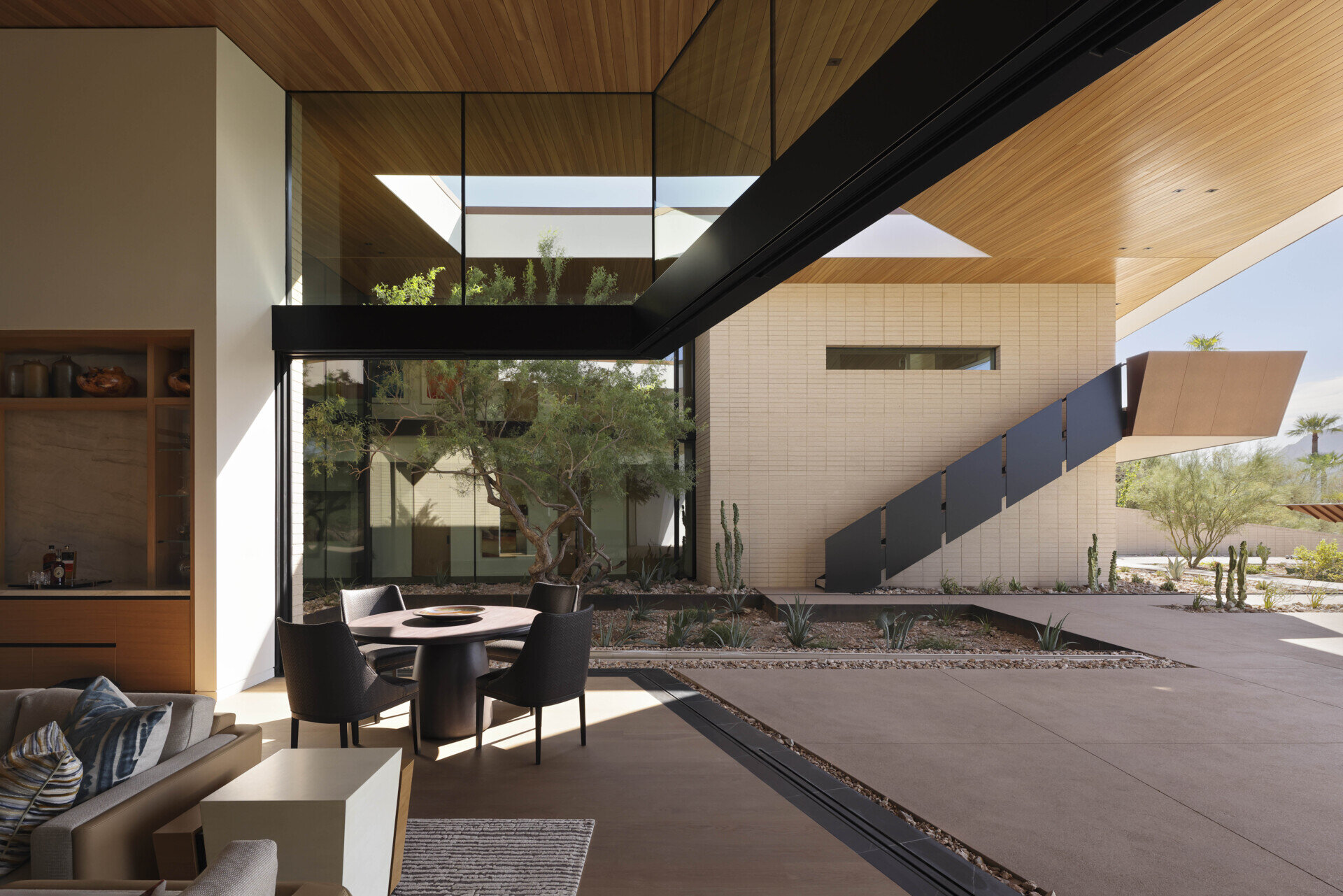 On the southern exposure, glass walls dissolve boundaries between indoors and out. The living spaces open to terraces, revealing a courtyard oasis where basins capture rainwater, sustaining lush greenery amid the arid surroundings.