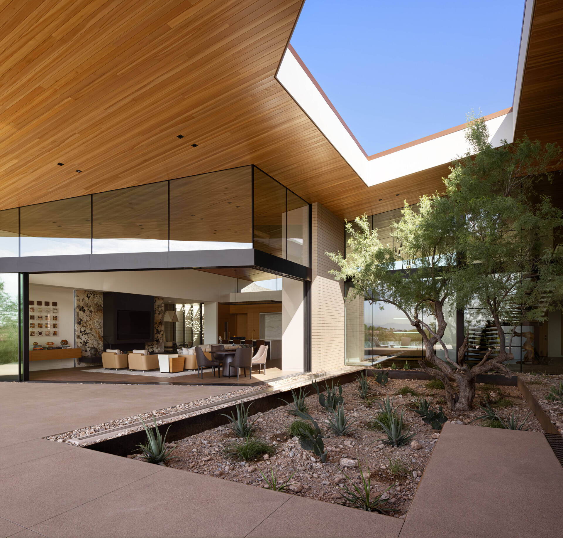 On the southern exposure, glass walls dissolve boundaries between indoors and out. The living spaces open to terraces, revealing a courtyard oasis where basins capture rainwater, sustaining lush greenery amid the arid surroundings.