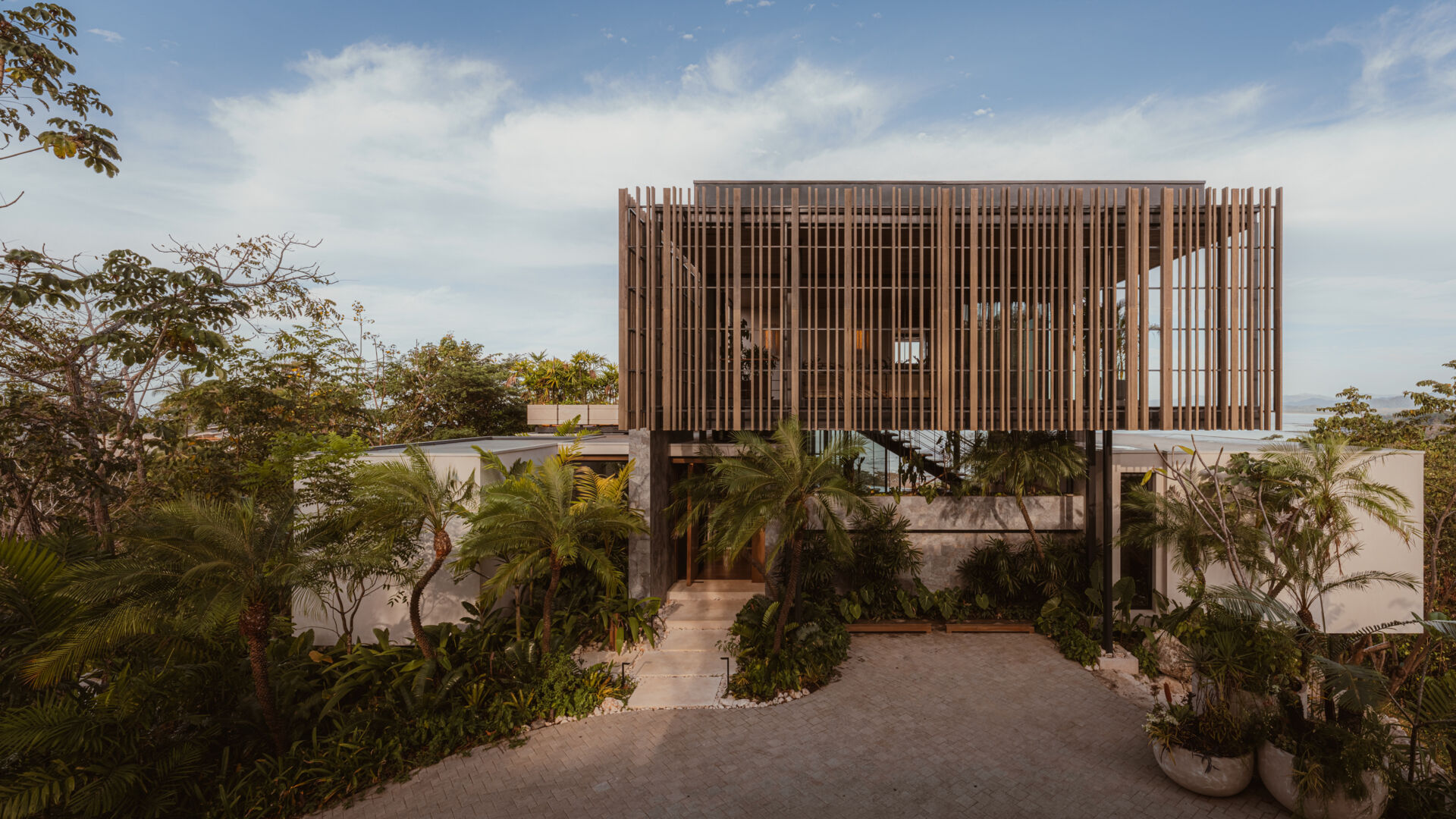 A modern house design with two pavilion-style volumes,  connected by a central vestibule, creates a layout that feels open, grounded, and deeply connected to the jungle canopy.