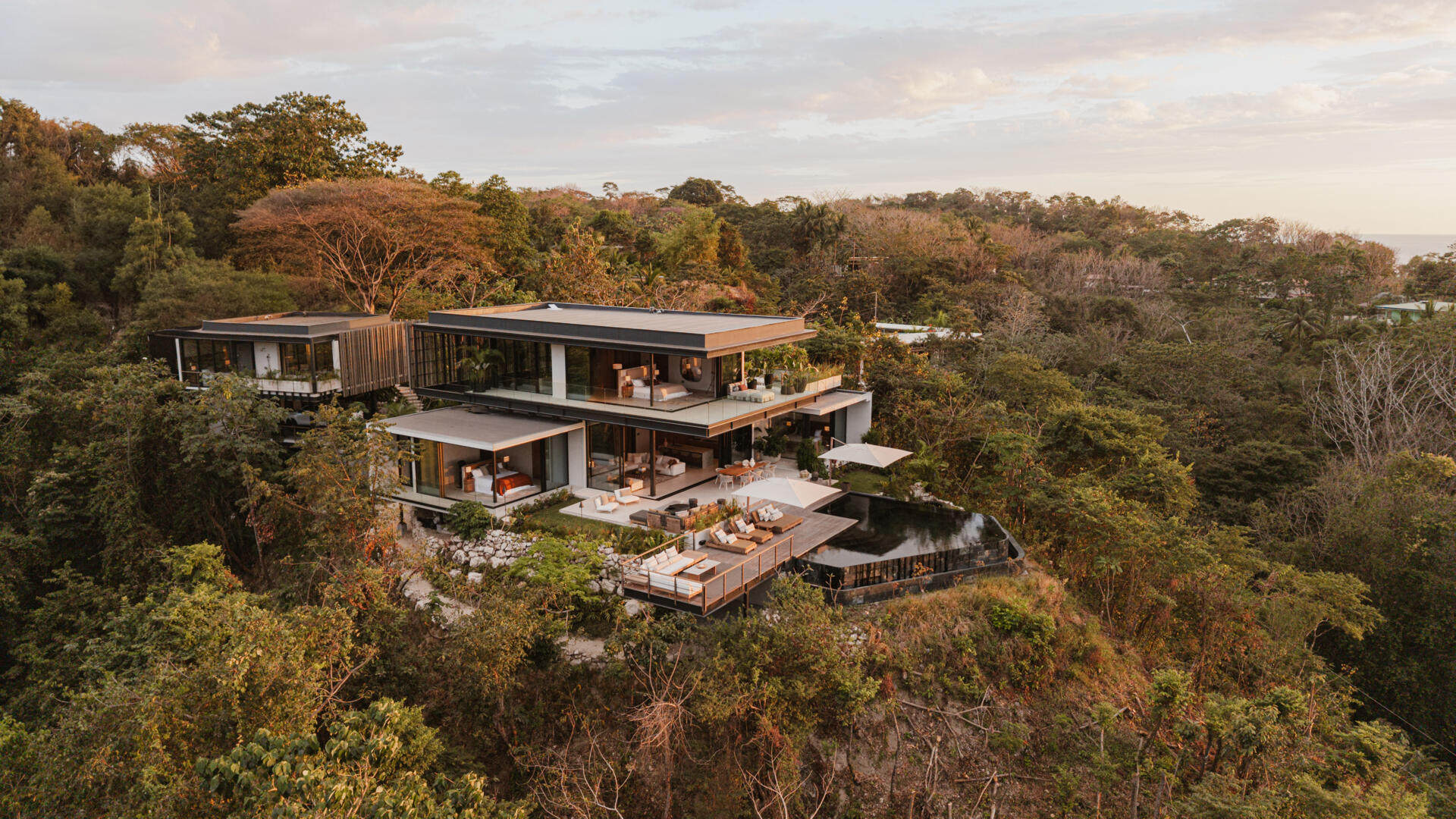 A modern house design with two pavilion-style volumes,  connected by a central vestibule, creates a layout that feels open, grounded, and deeply connected to the jungle canopy.
