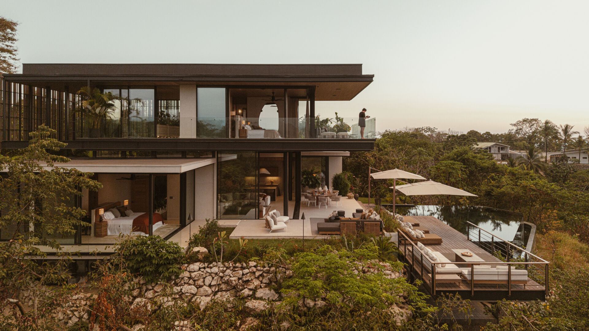 A modern house design with two pavilion-style volumes,  connected by a central vestibule, creates a layout that feels open, grounded, and deeply connected to the jungle canopy.
