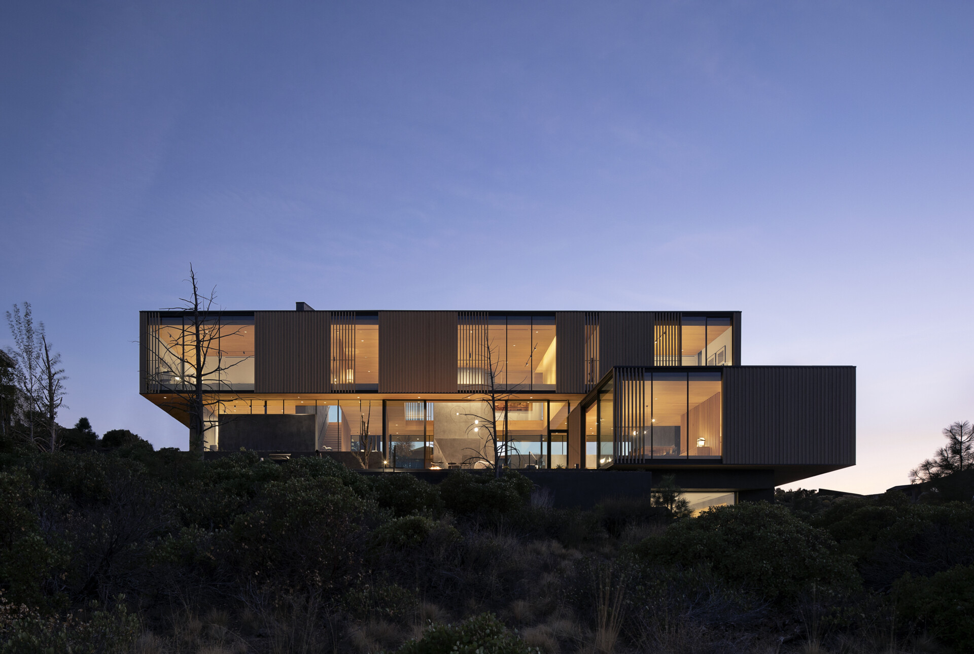 This modern home is designed as a series of cascading platforms that step down a pumice-covered hillside. Inspired by nearby volcanic rock formations, faceted mass walls anchor the structure, guiding movement and framing both intimate and expansive views. 
