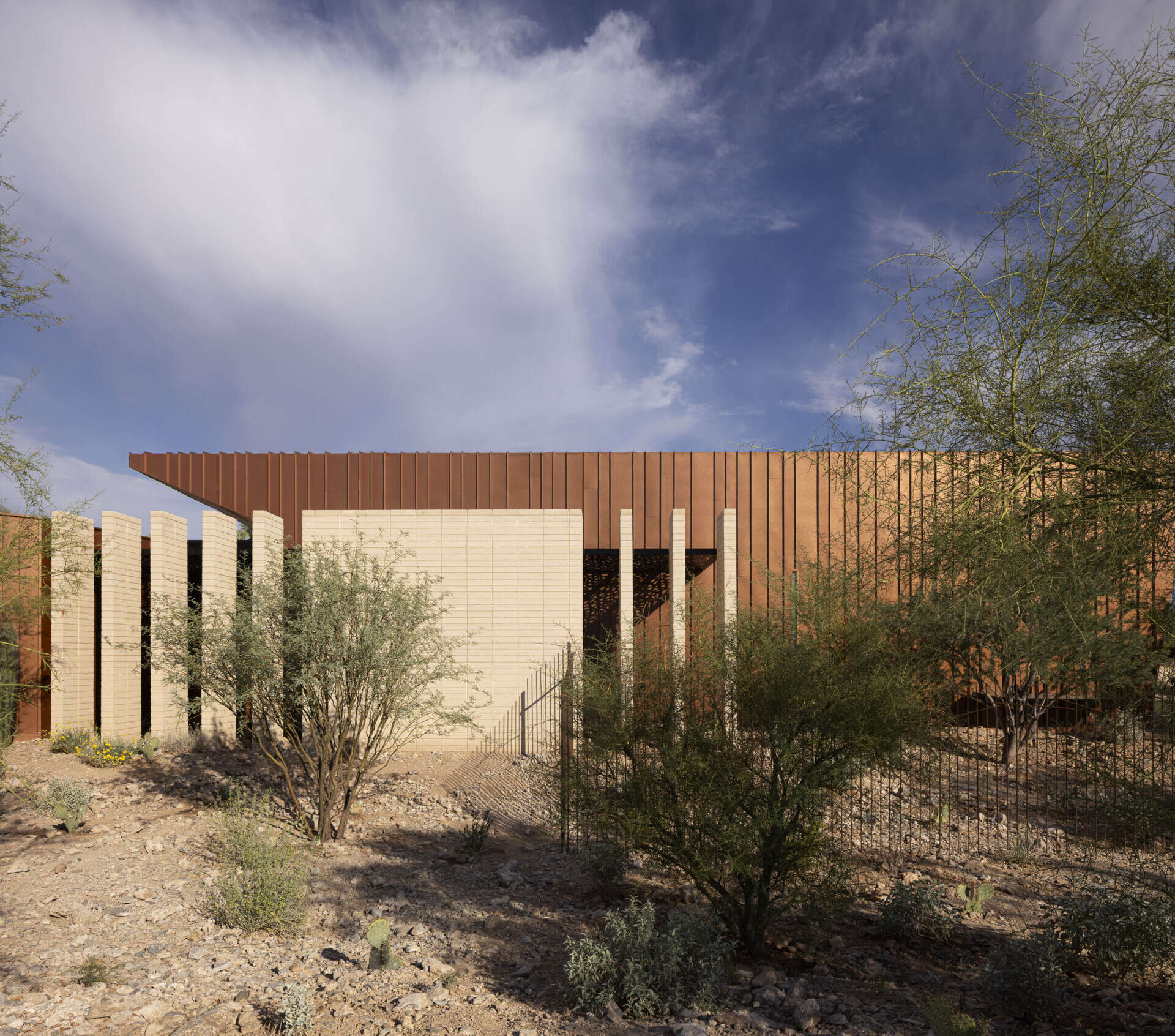 Defined by folding metal planes and rugged blasted-face masonry, the architecture of this modern house recalls the layered beauty of a geode. The weathered metal acts as a protective shell, sheltering the glass-filled interior that glows with natural daylight.