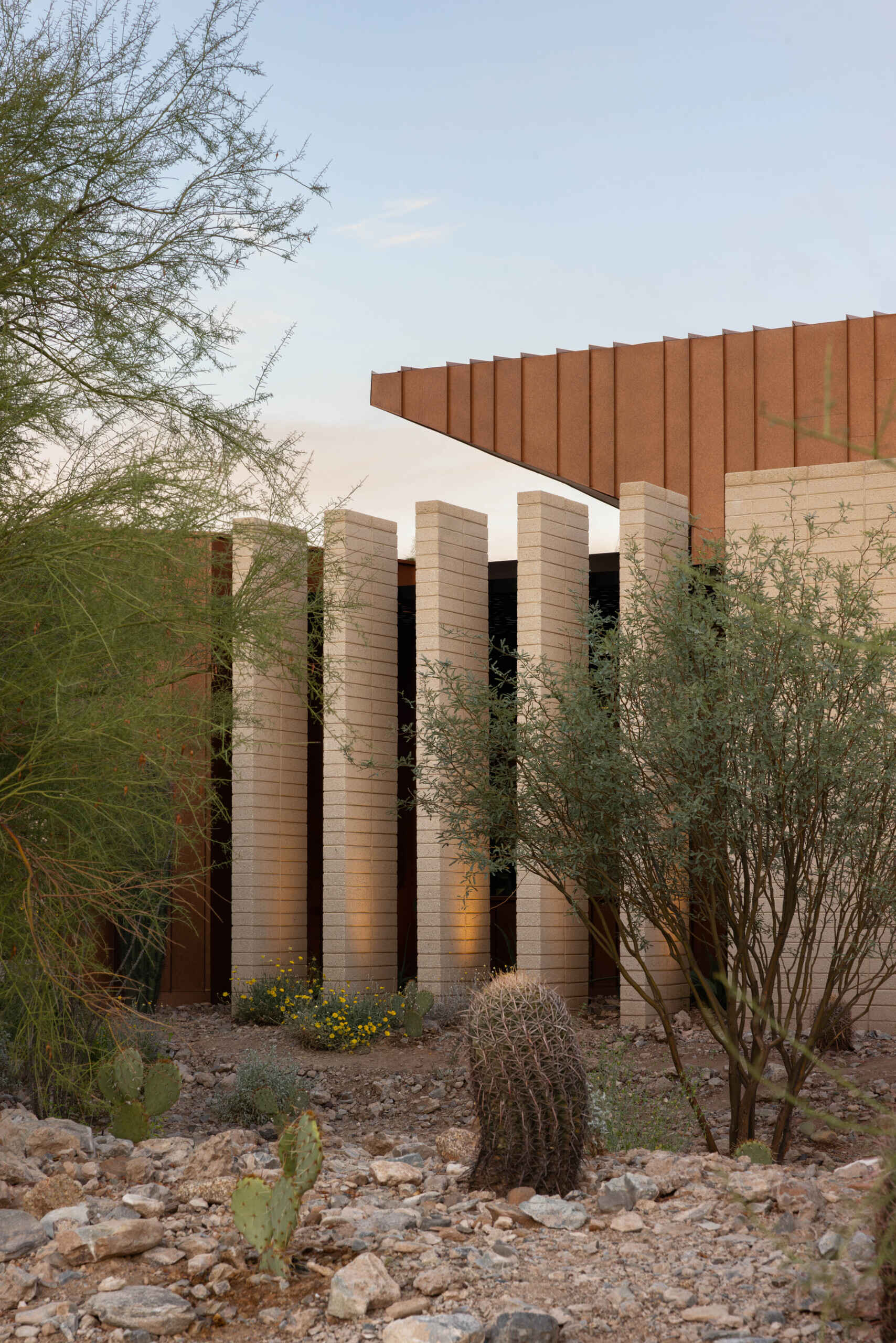 Defined by folding metal planes and rugged blasted-face masonry, the architecture of this modern house recalls the layered beauty of a geode. The weathered metal acts as a protective shell, sheltering the glass-filled interior that glows with natural daylight.